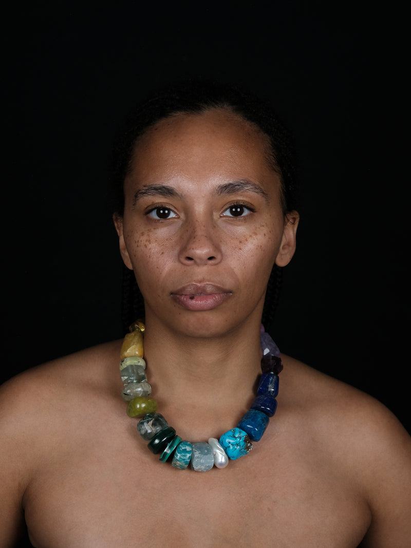 A multicolor gemstone beaded necklace, worn by a female model against a black background.
