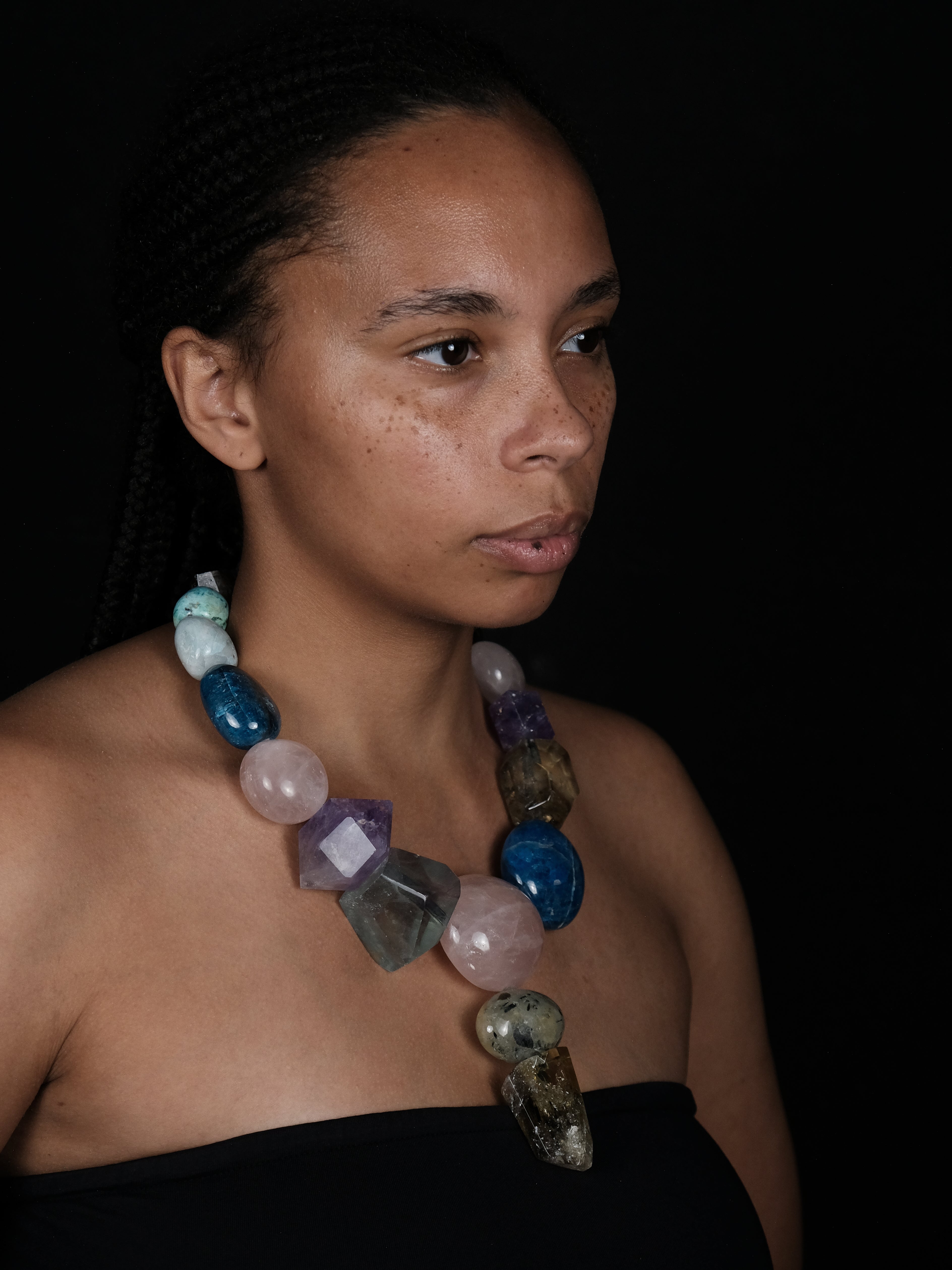 A woman wearing A multicolor beaded necklace featuring faceted gemstone beads in shades of pink, light blue, purple, amber, and clear, with a teardrop-shaped light blue stone pendant hanging from the center.