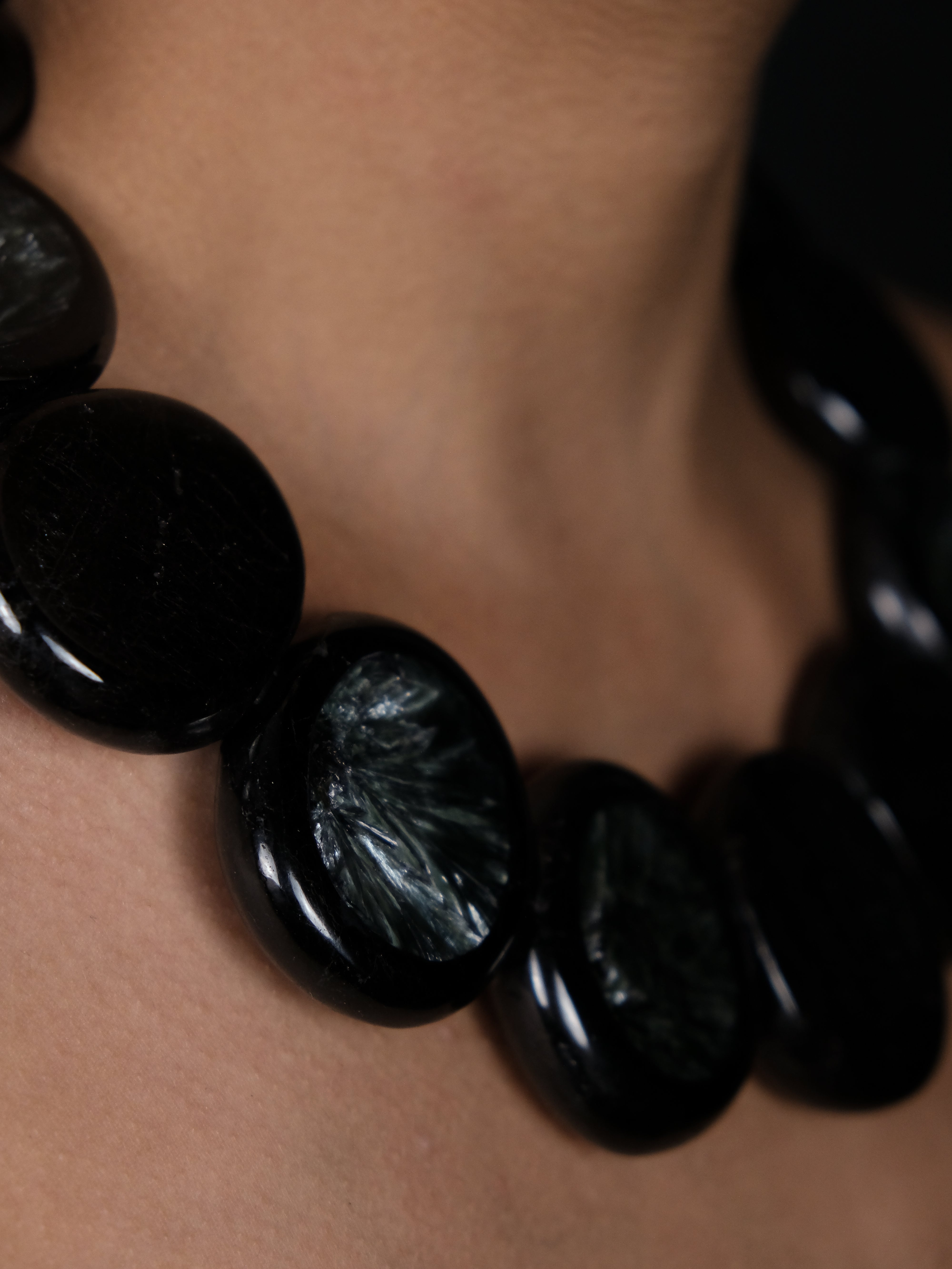 A close-up of a person wearing a chunky black beaded necklace made of polished, glossy disc-shaped beads with a subtle iridescent sheen.