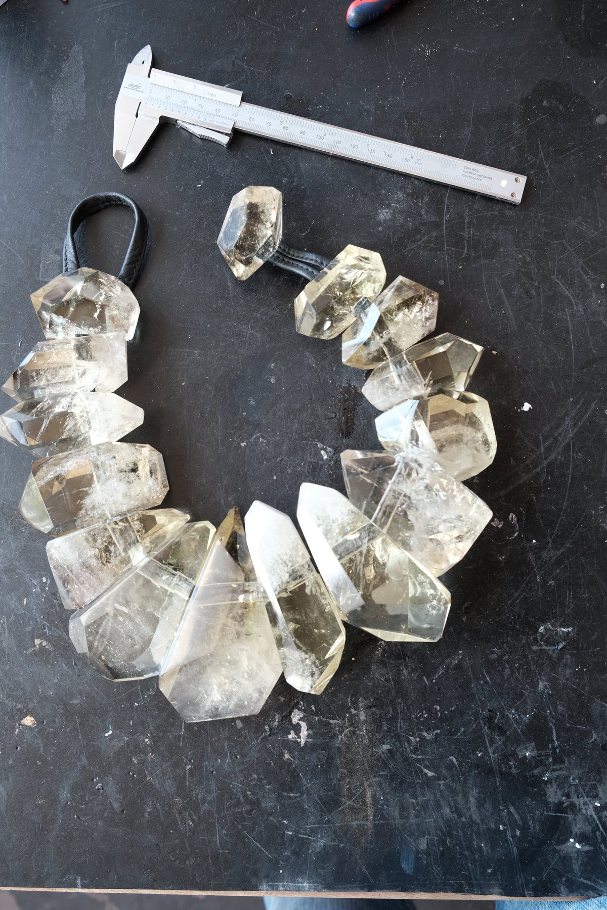 A handmade crystal bead necklace made of faceted yellow citrne points on a black background, shown next to a metal caliper for scale.