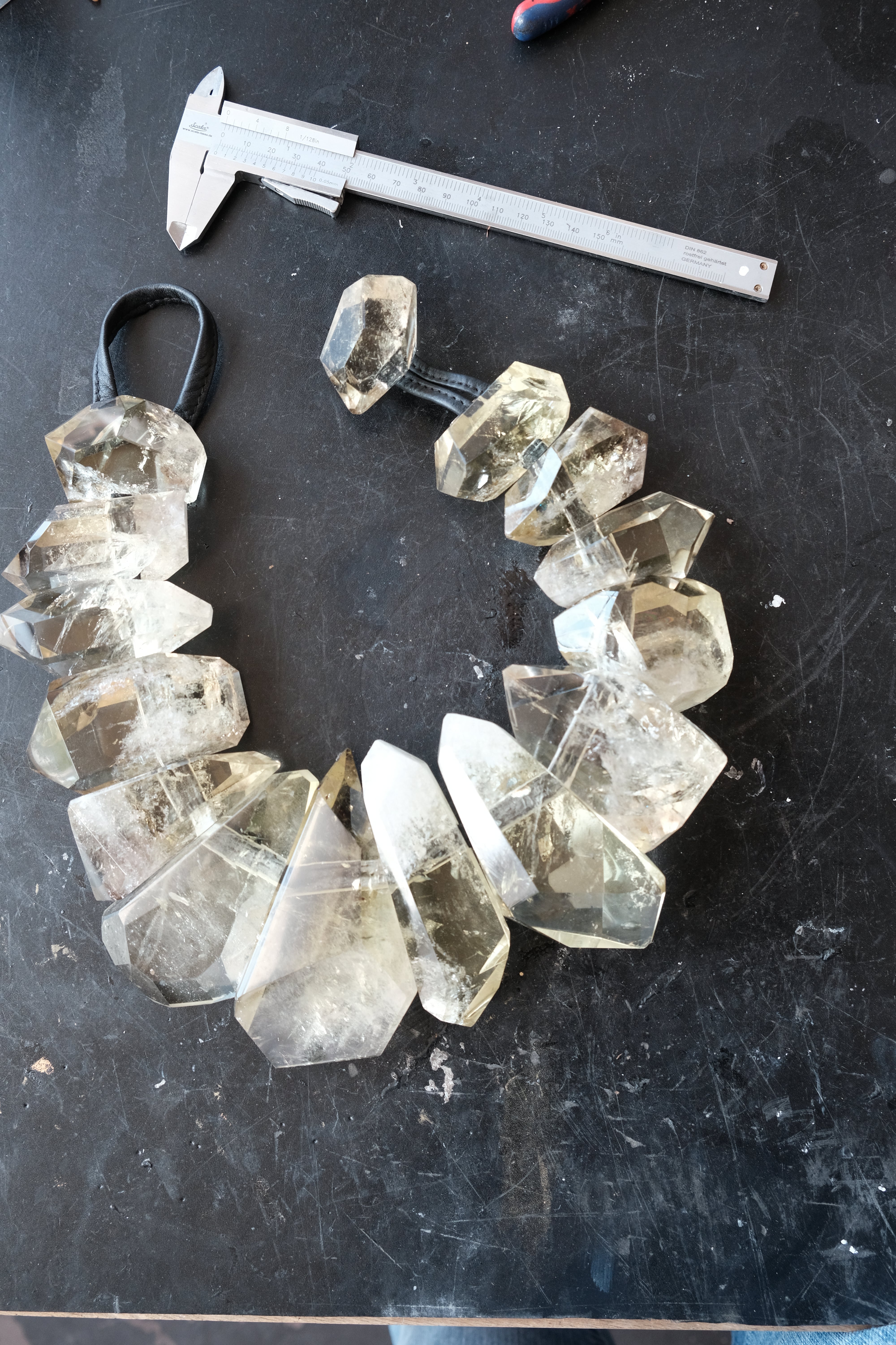 A handmade crystal bead necklace made of faceted yellow citrne points on a black background, shown next to a metal caliper for scale.