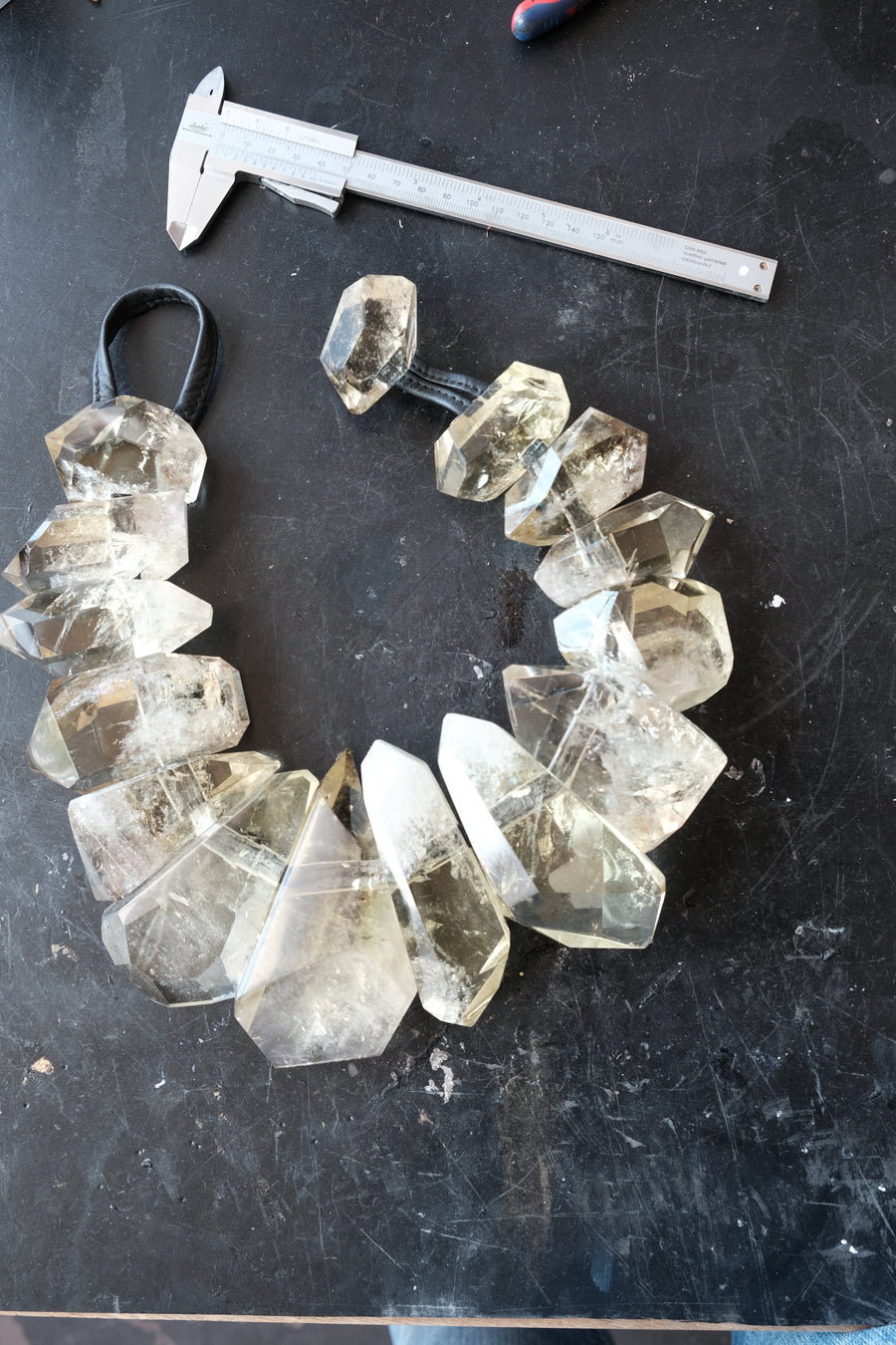 A handmade crystal bead necklace made of faceted yellow citrne points on a black background, shown next to a metal caliper for scale.