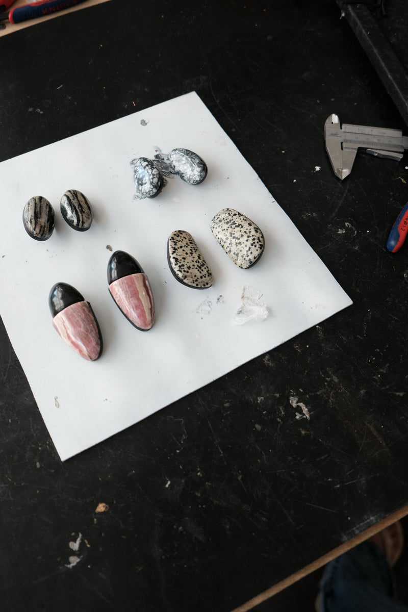 Several polished decorative stones and small polished stone pieces arranged on a white sheet over a dark workbench, with a caliper visible in the upper right.