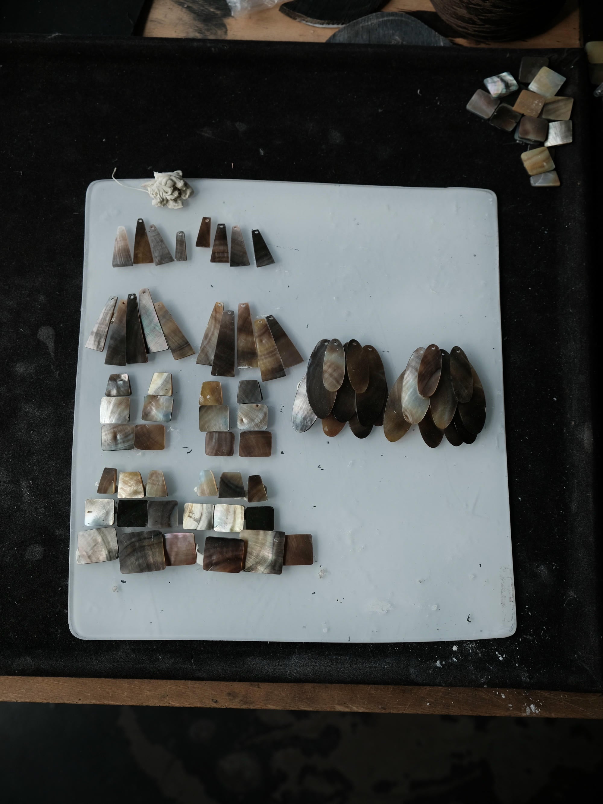 A collection of handmade jewelry components, including various cone-shaped and rectangular pieces made from natural mother-of-pearl and brown stone, neatly arranged on a white cutting board.