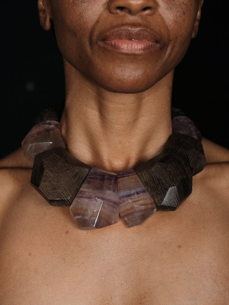 Close-up of a person wearing a geometric stone necklace against a dark background