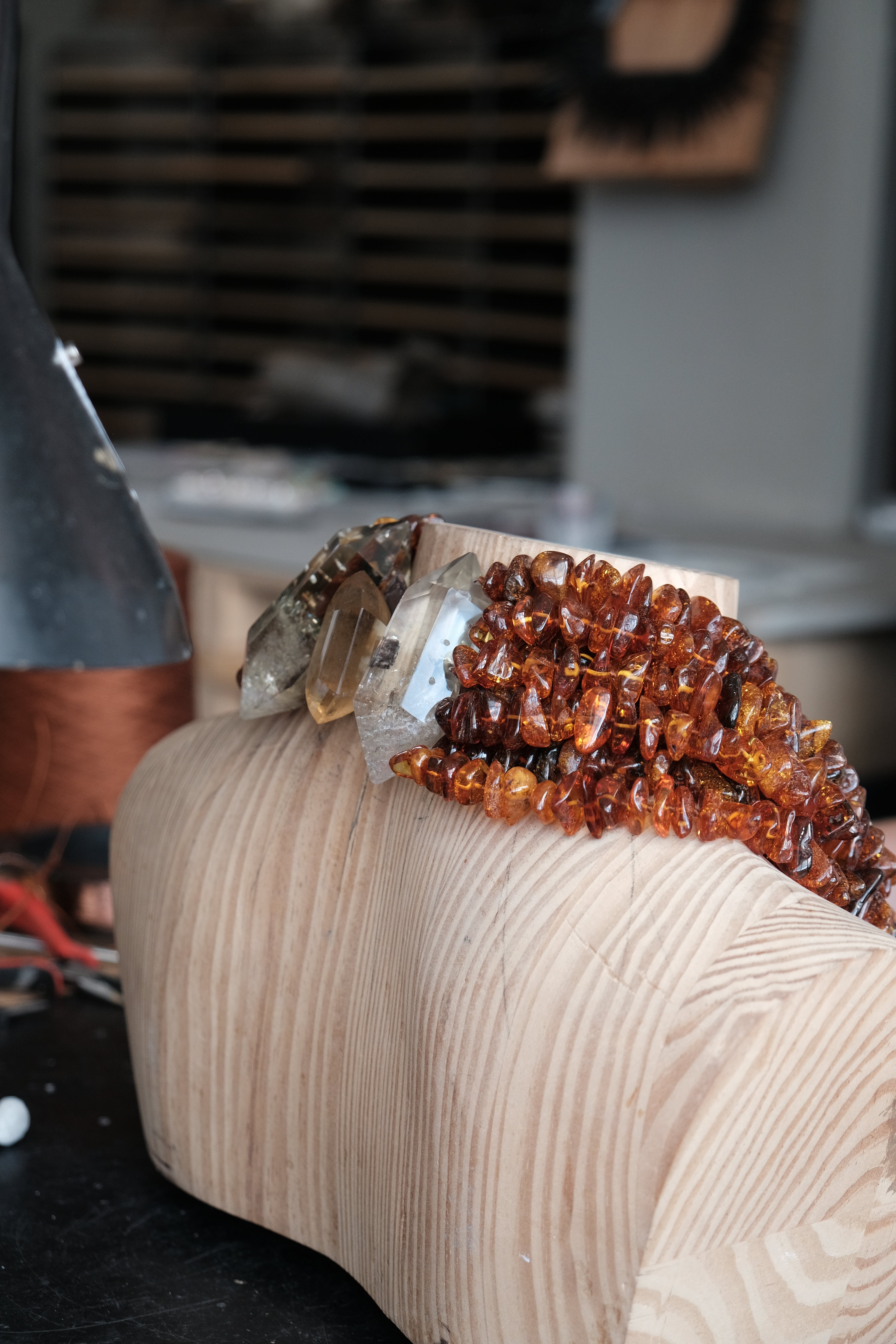 A close-up of a carved wooden sculpture or block with a cluster of amber and clear crystals resting on top, photographed in a workshop setting.