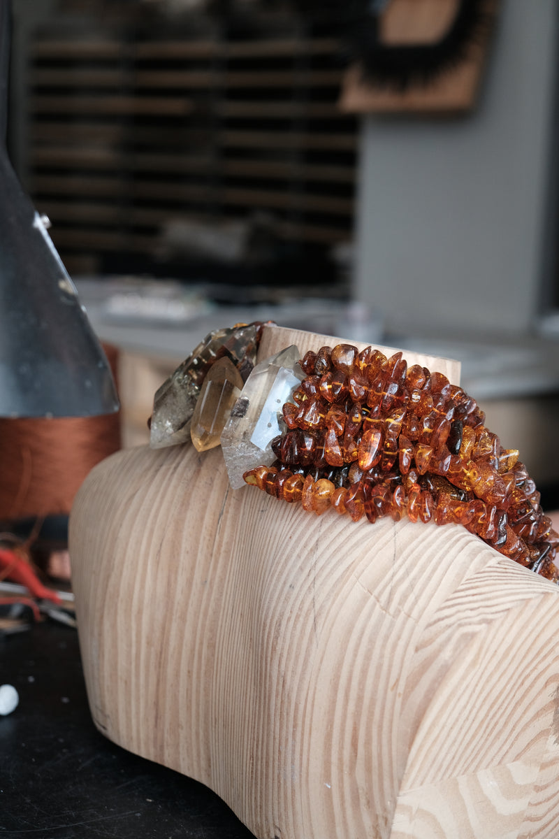 A close-up of a carved wooden sculpture or block with a cluster of amber and clear crystals resting on top, photographed in a workshop setting.
