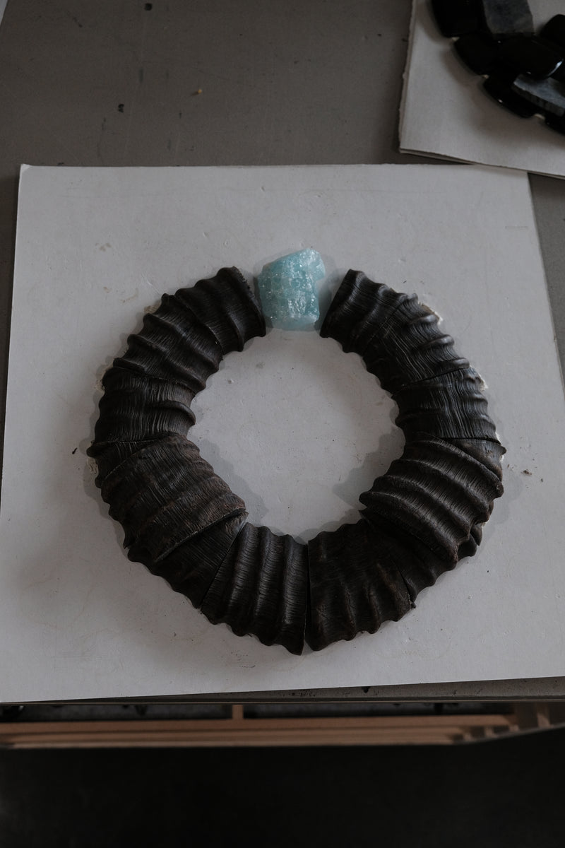 Horn necklace with an aquamarine stone, displayed on a white workbench