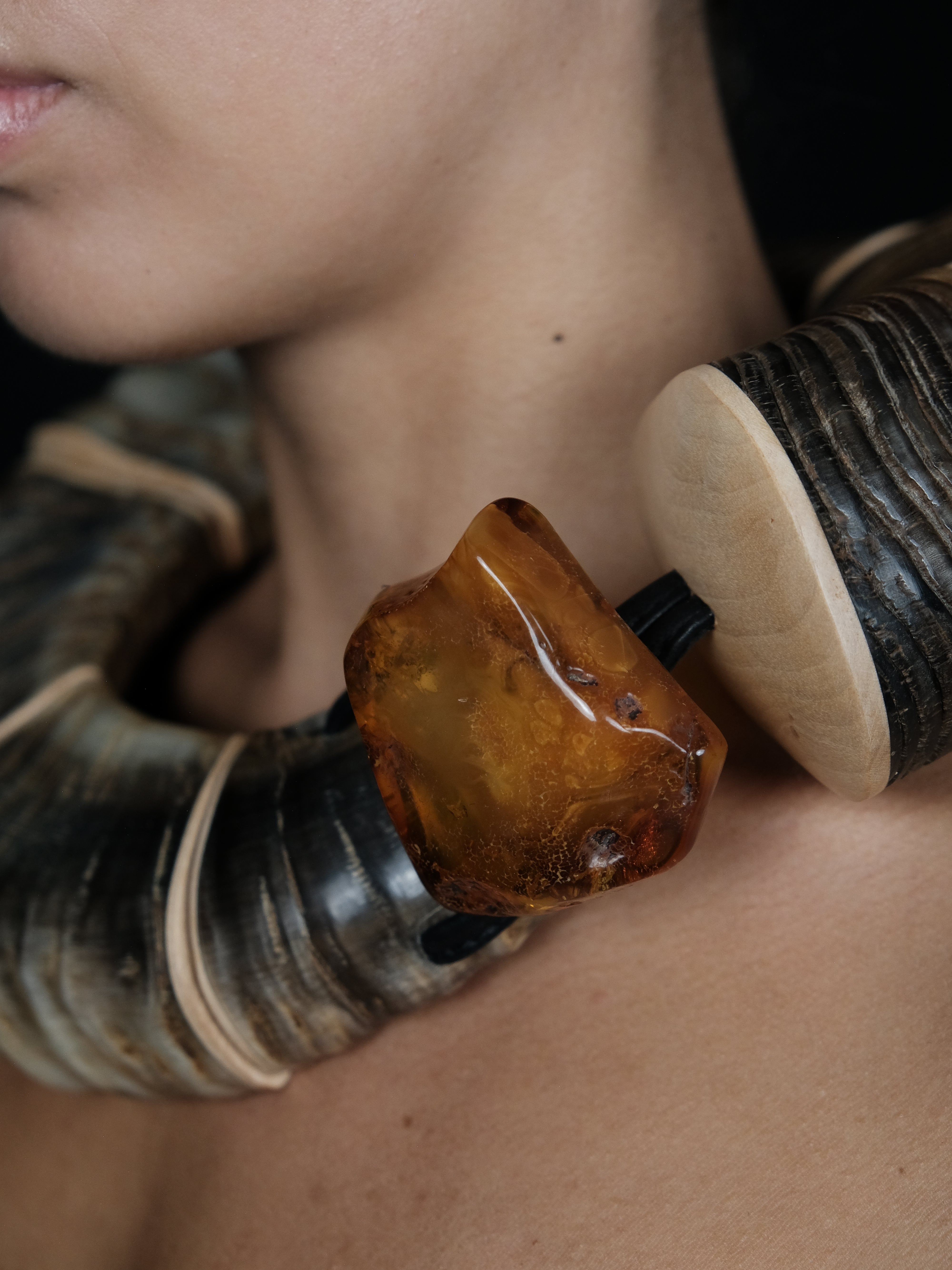 A close-up of a person wearing a chunky collar necklace made of dark horn, wood and polished amber pieces.