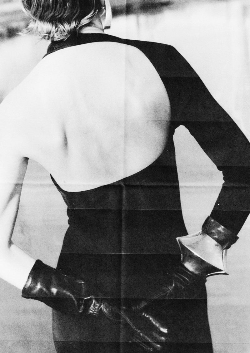 A black and white image of a person wearing a sleeveless top and black gloves, with the focus on the bracelet around the wrist.