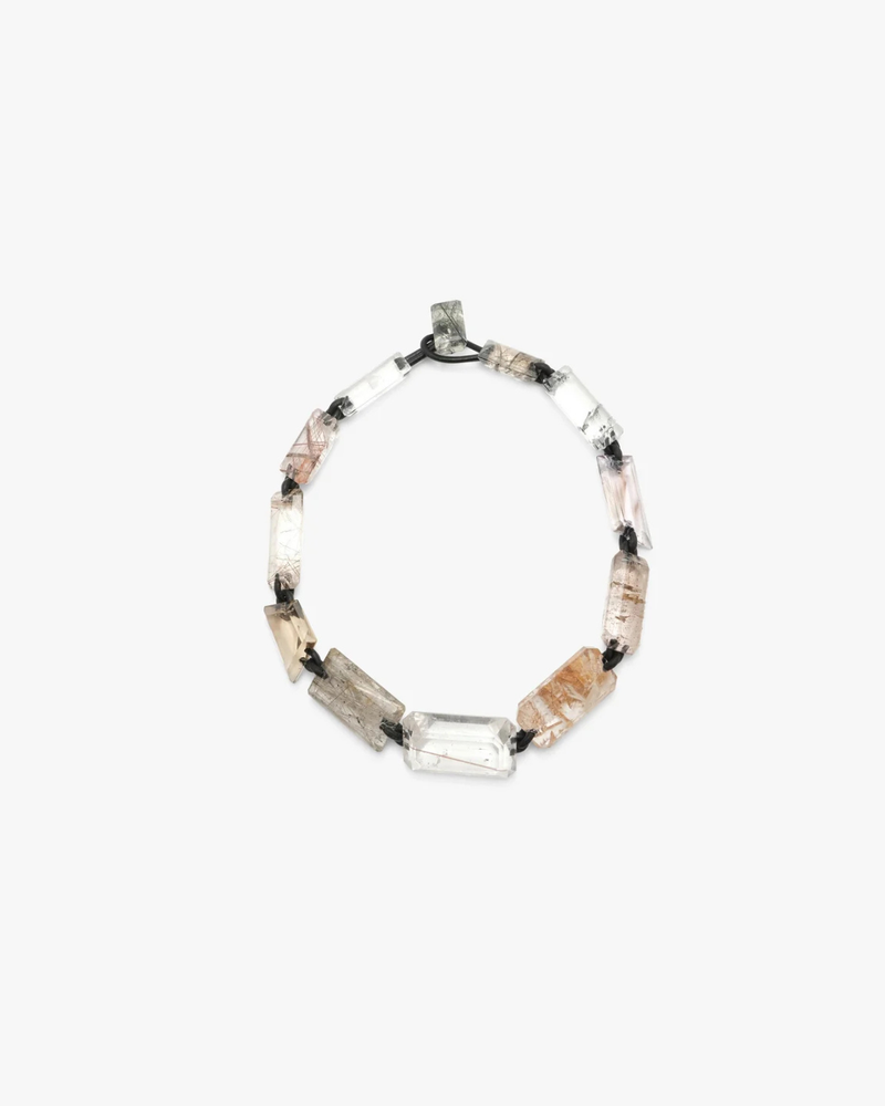 A beaded necklace featuring clear quartz, , and smoky brown stone segments separated by small black beads, displayed on a light gray background.
