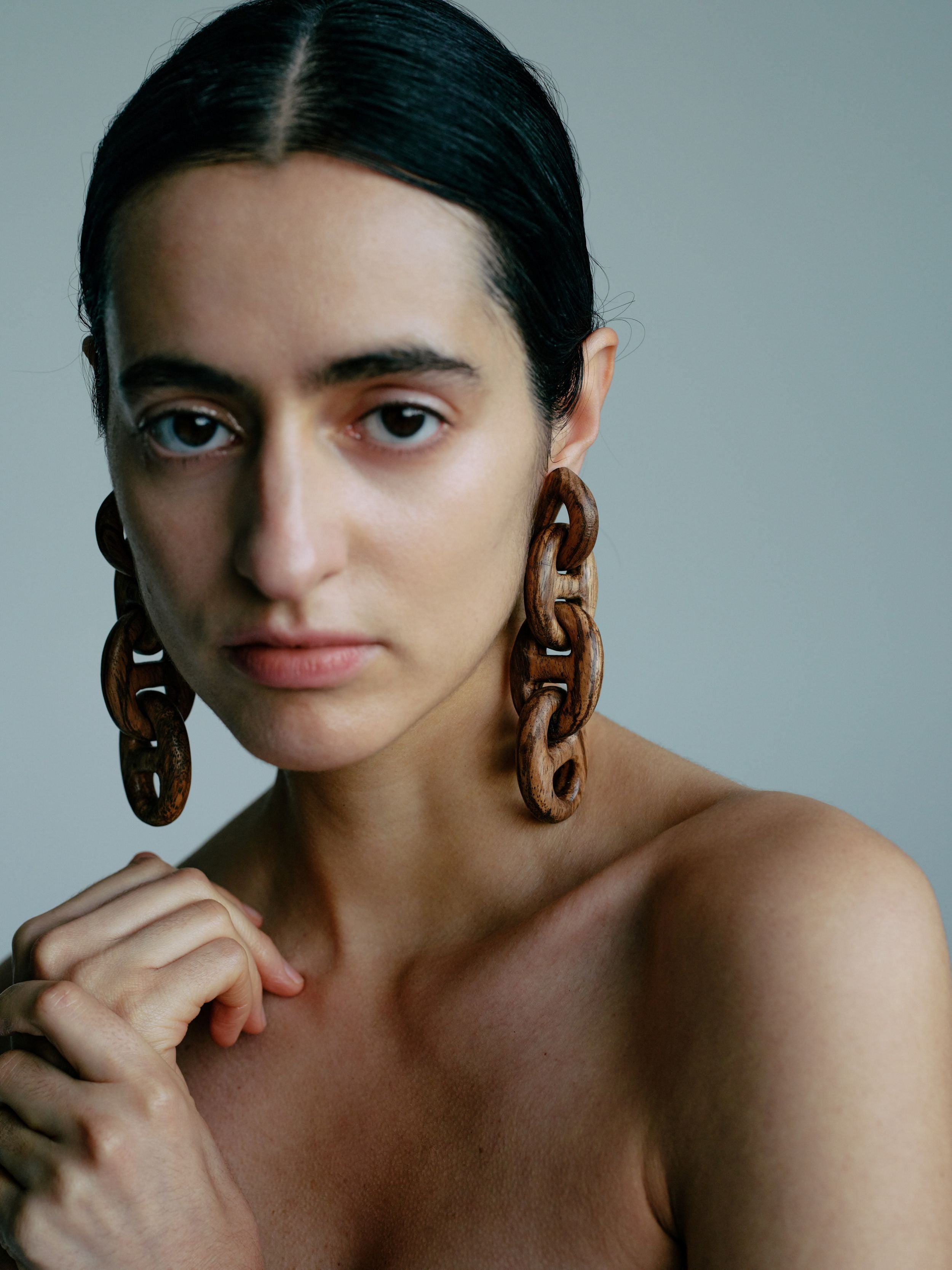 Woman wearing large chain earrings against a neutral background