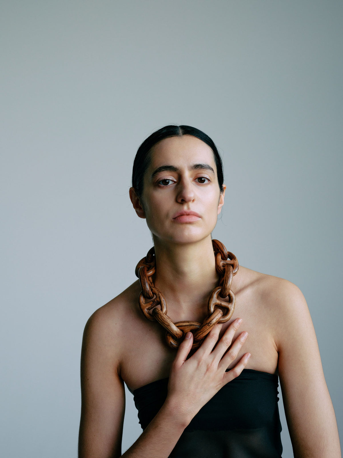 Woman wearing a large, wooden necklace against a plain background