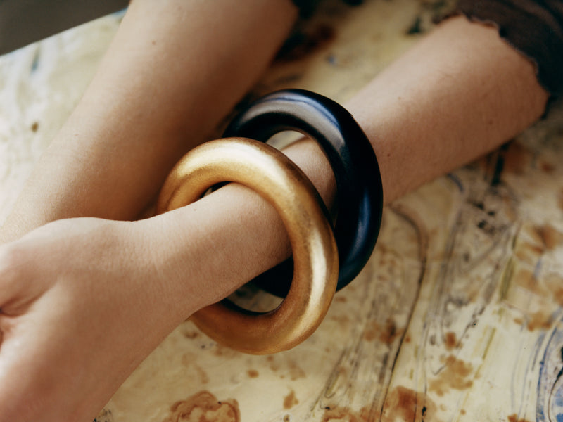 Close-up of a person's arm with gold and black bangles on a patterned surface