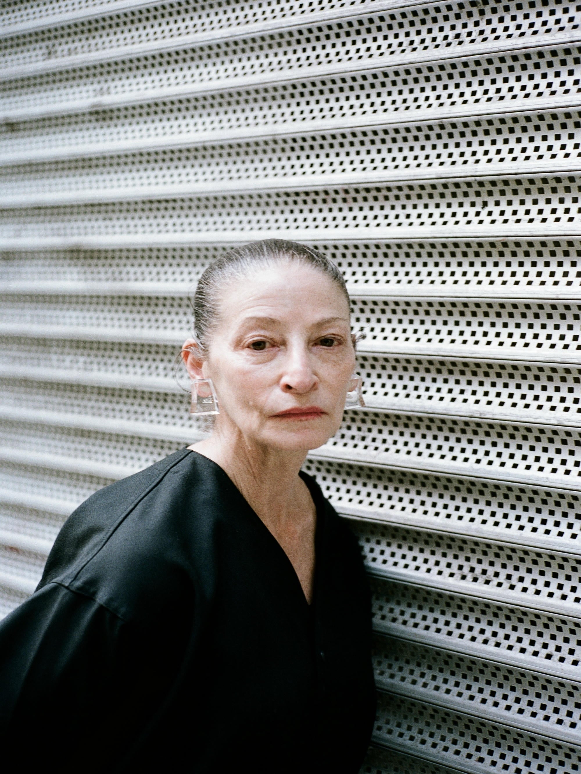 Woman in a black outfit standing against a textured white wall