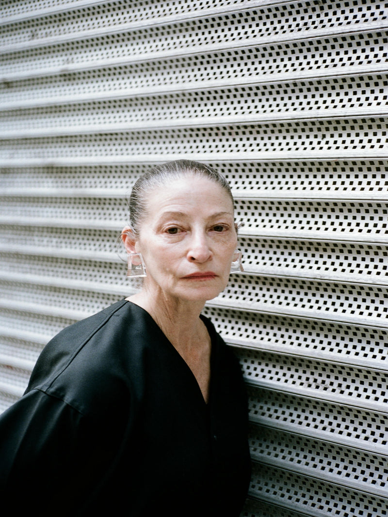 Woman in a black outfit standing against a textured white wall