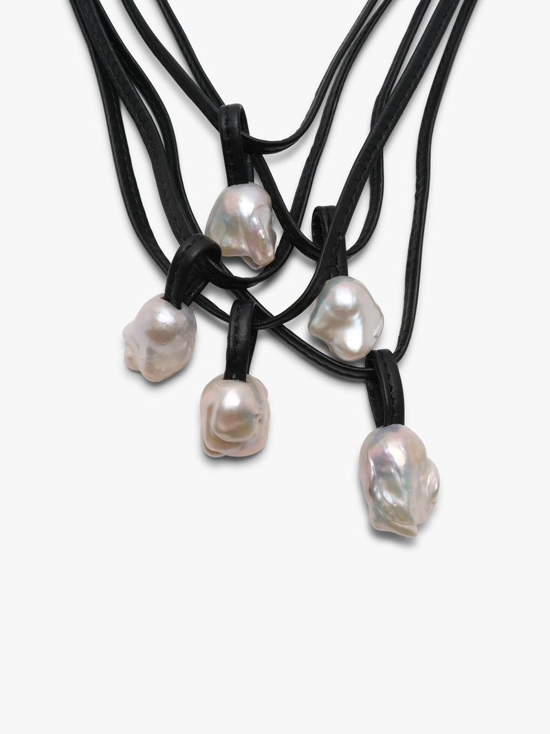 Close up of a necklace with white baroque pearls and leather straps, featuring a toggle clasp lock.