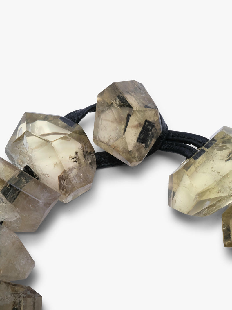 A close-up of a beaded necklace featuring faceted, yellow citrine beads with natural inclusions, threaded on a black elastic band, set against a plain white background.
