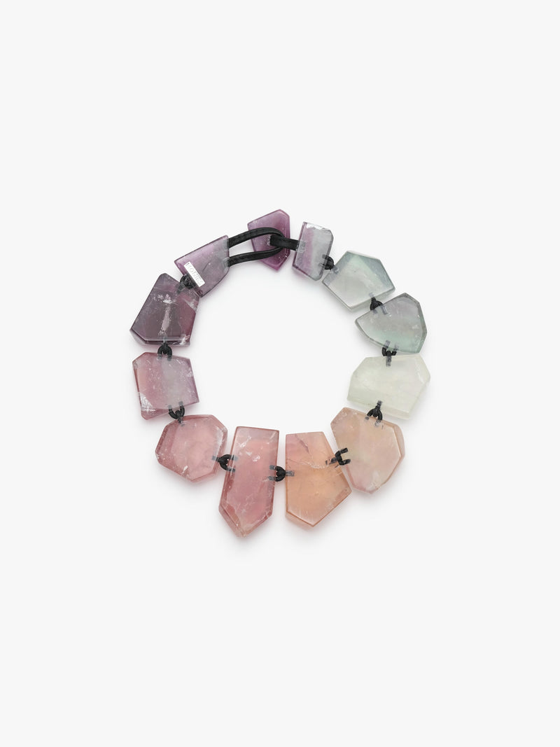 A necklace made of irregular, faceted gemstone beads in a gradient of colors from pale green and white to pink and deep purple, strung on a black elastic band, shown against a plain white background.