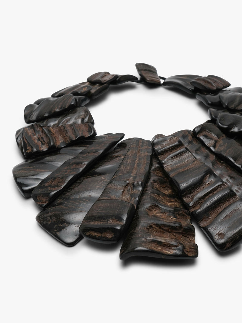 A dark brown horn statement necklace with layered, fan-shaped pieces and a small rectangular clasp, shown on a plain light gray background.