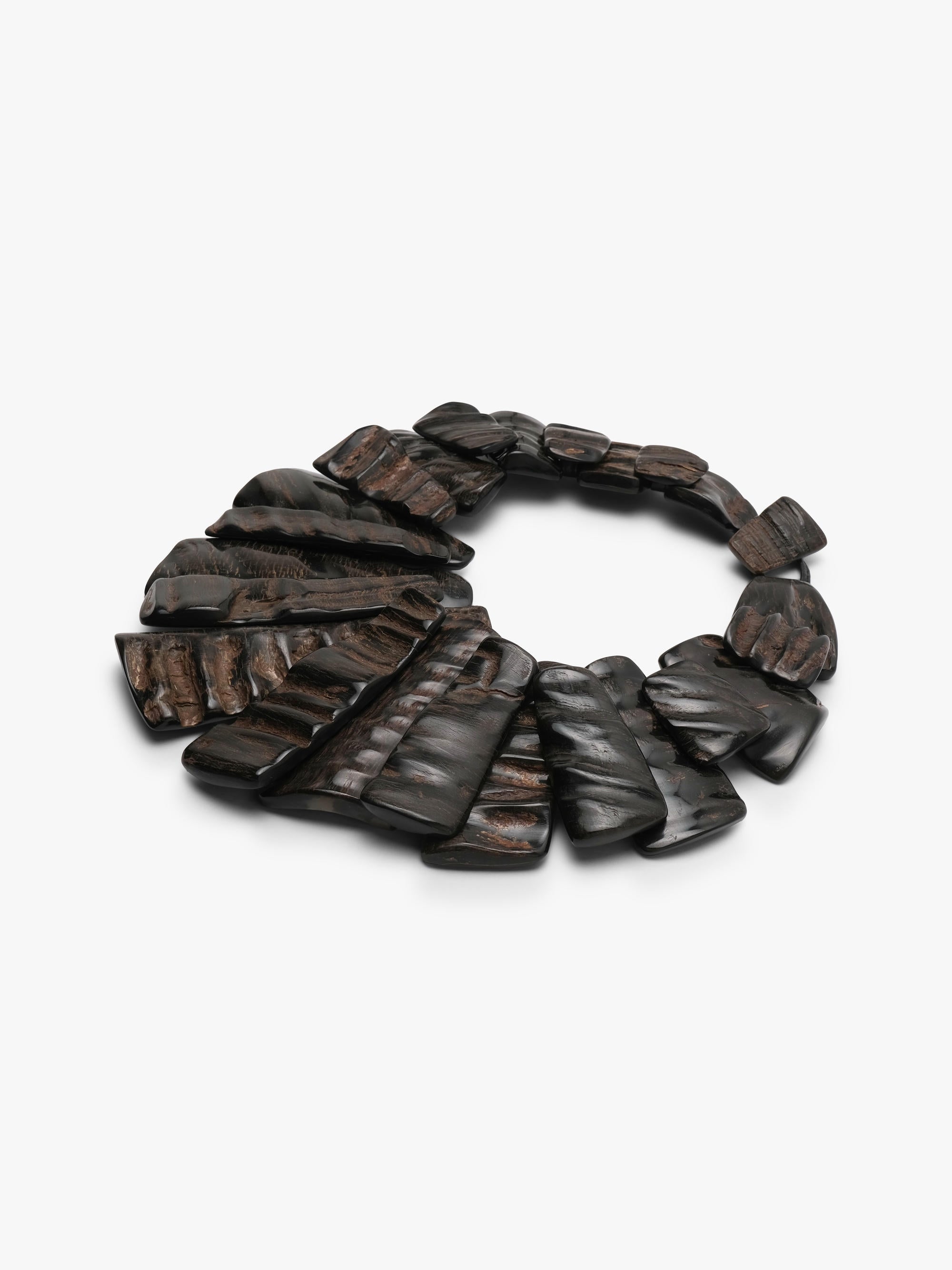 A dark brown horn statement necklace with layered, fan-shaped pieces and a small rectangular clasp, shown on a plain light gray background.
