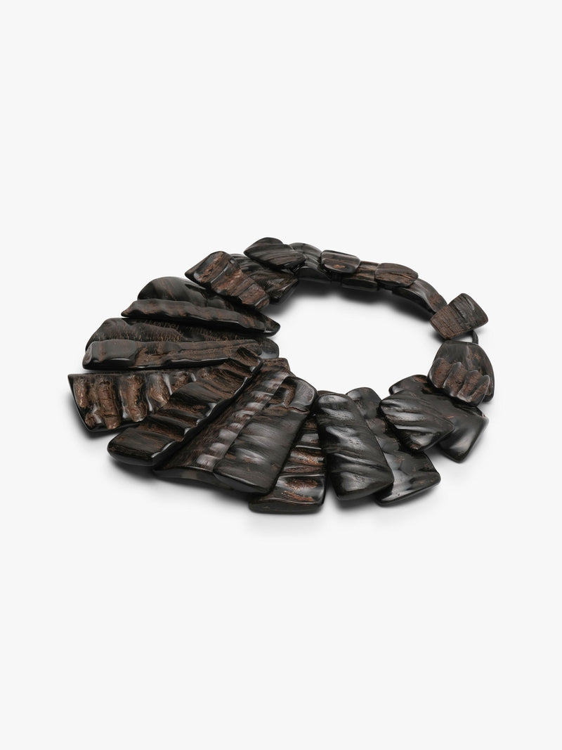 A dark brown horn statement necklace with layered, fan-shaped pieces and a small rectangular clasp, shown on a plain light gray background.