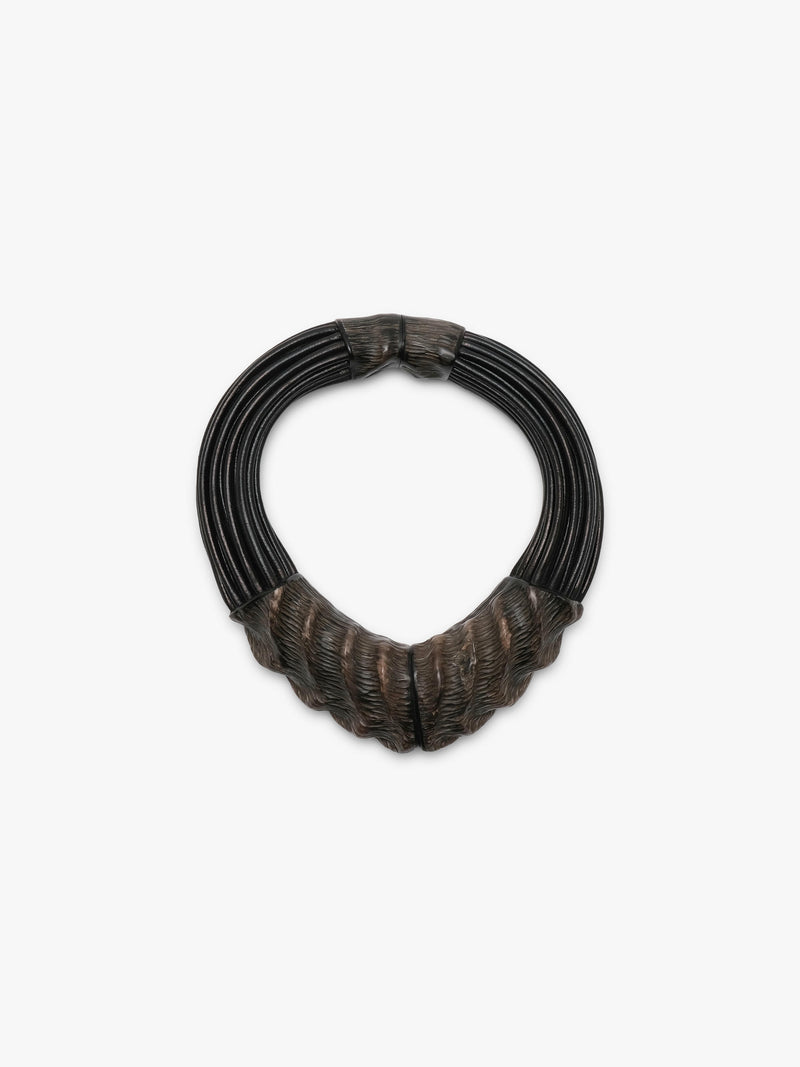 A dark multi-strand collar necklace with textured, horn sculpted ends and black leather cords, shown on a plain light gray background.