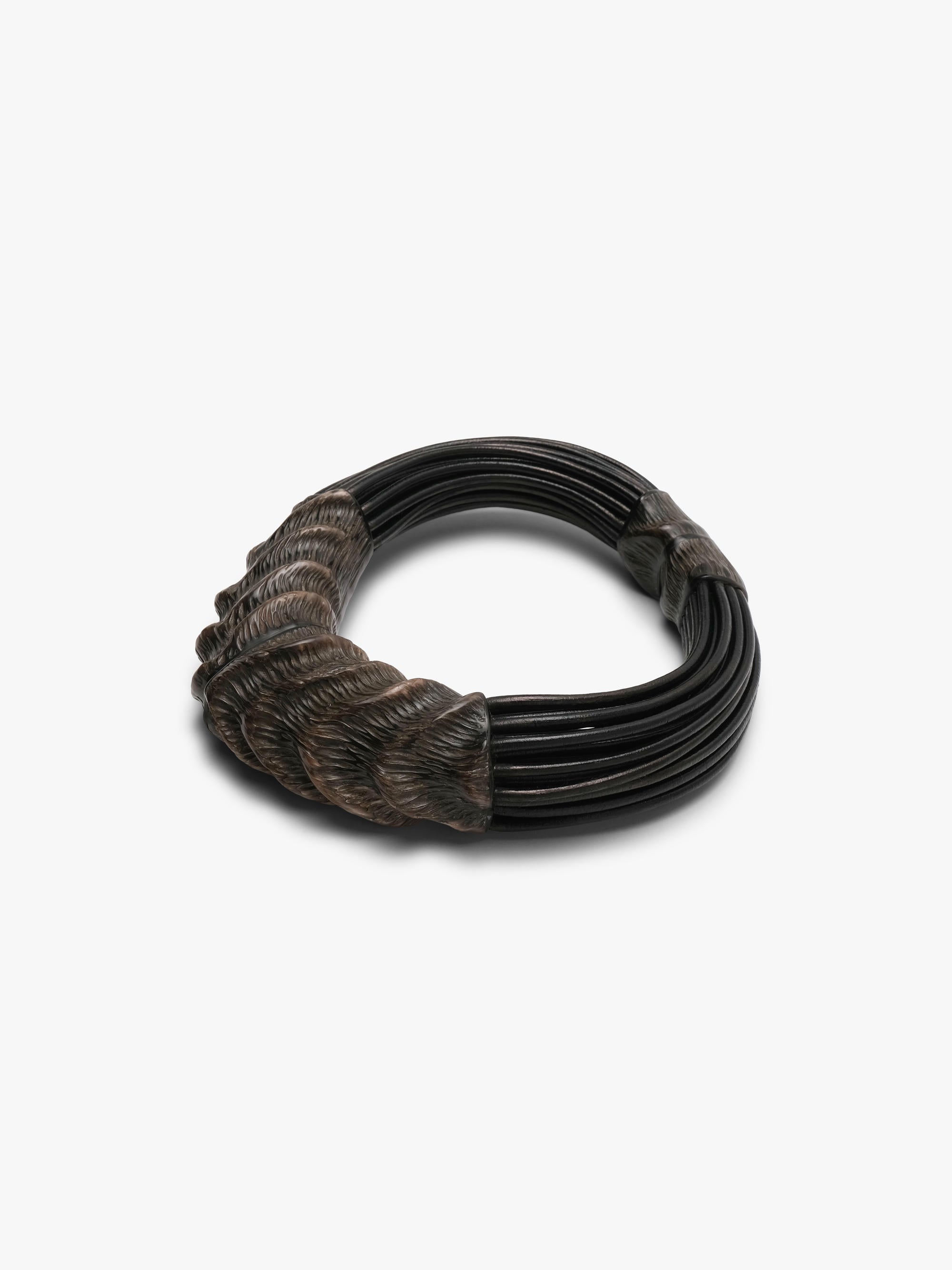 A dark multi-strand collar necklace with textured, horn sculpted ends and black leather cords, shown on a plain light gray background.