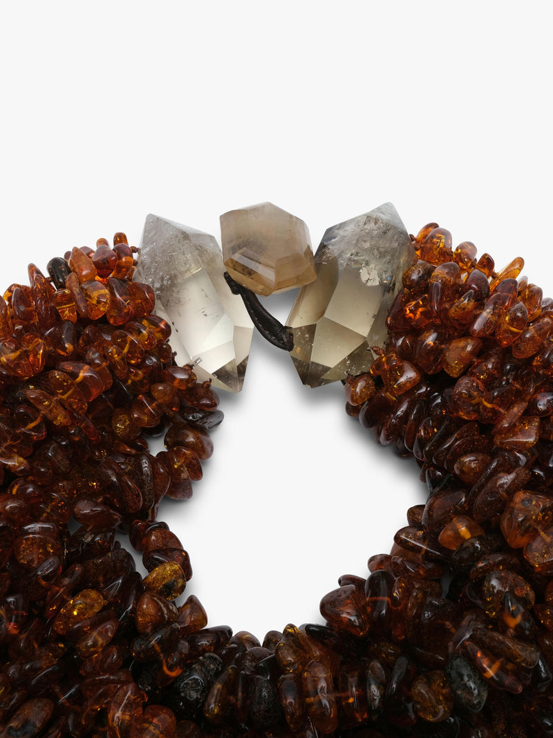 A chunky multi-strand amber necklace made of small, irregular brown amber pieces, accented with three raw citrine crystal beads in white, smoky gray, and light brown, set against a plain white background.