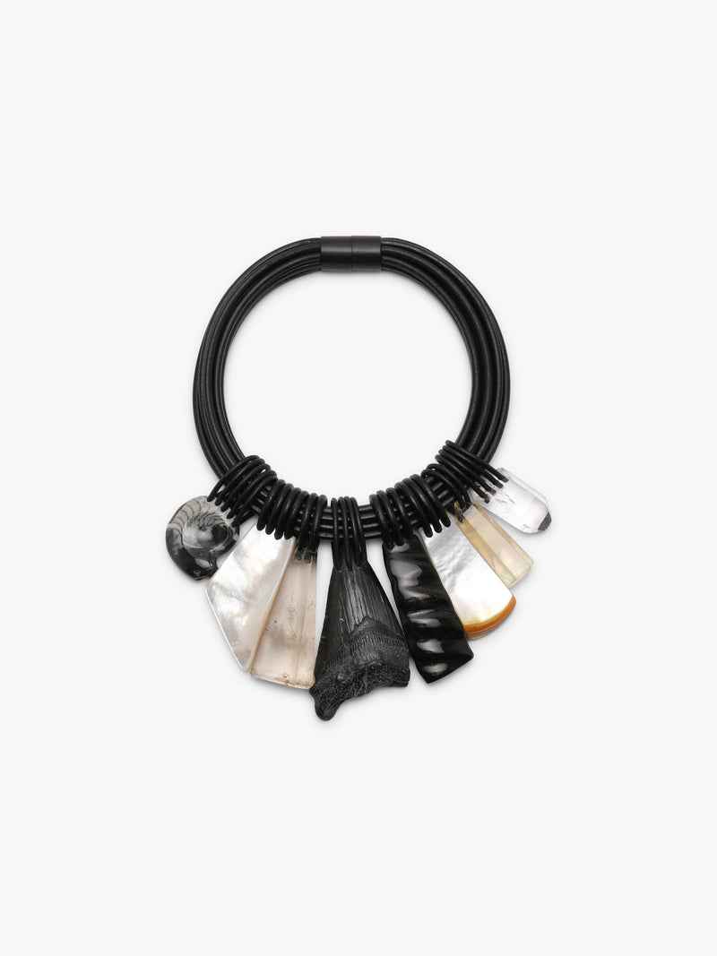 A black coiled cord bracelet with multiple natural stone and shell charms, including a black shark fin, a white cowrie shell, a small orange piece, and a clear crystal, displayed on a clean white background.