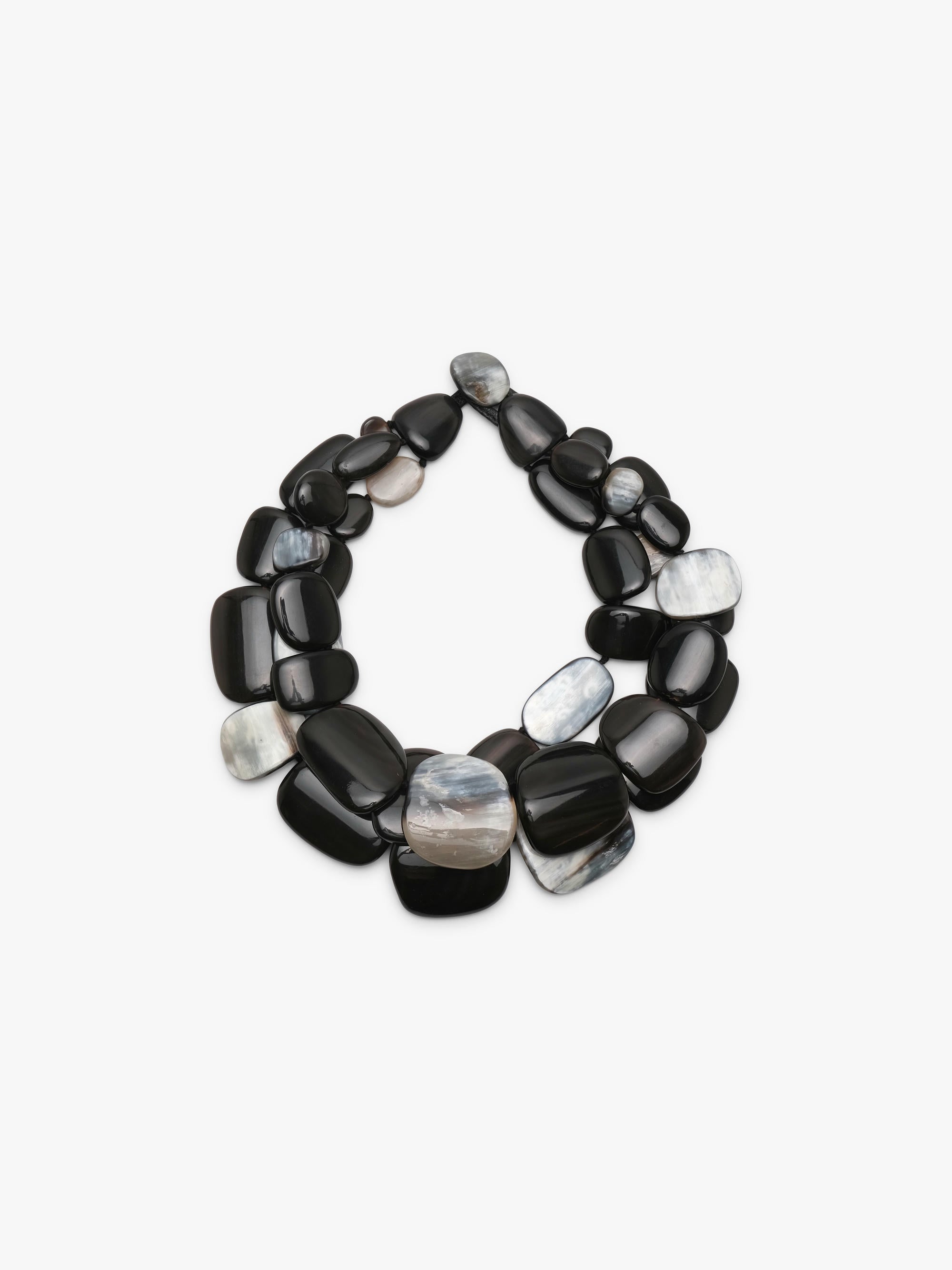 A statement collar necklace made of polished, smooth pebble-shaped horn in black, dark gray with iridescent white and gray patterns, displayed on a clean white background.