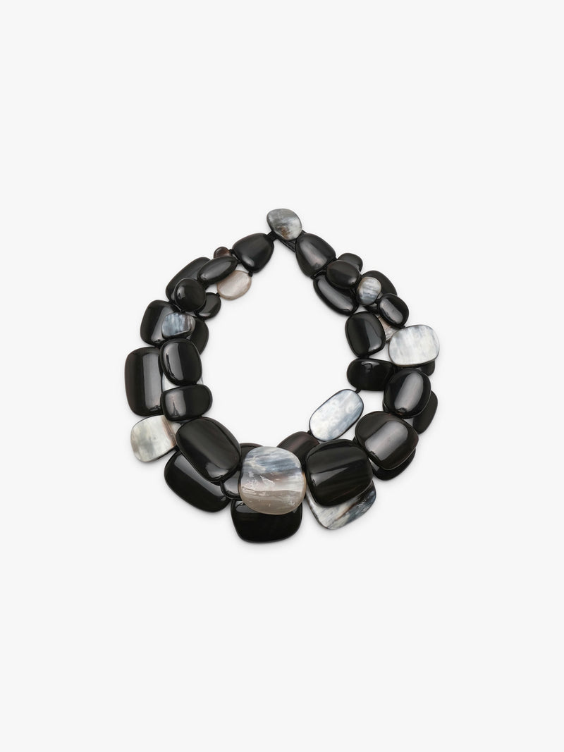 A statement collar necklace made of polished, smooth pebble-shaped horn in black, dark gray with iridescent white and gray patterns, displayed on a clean white background.