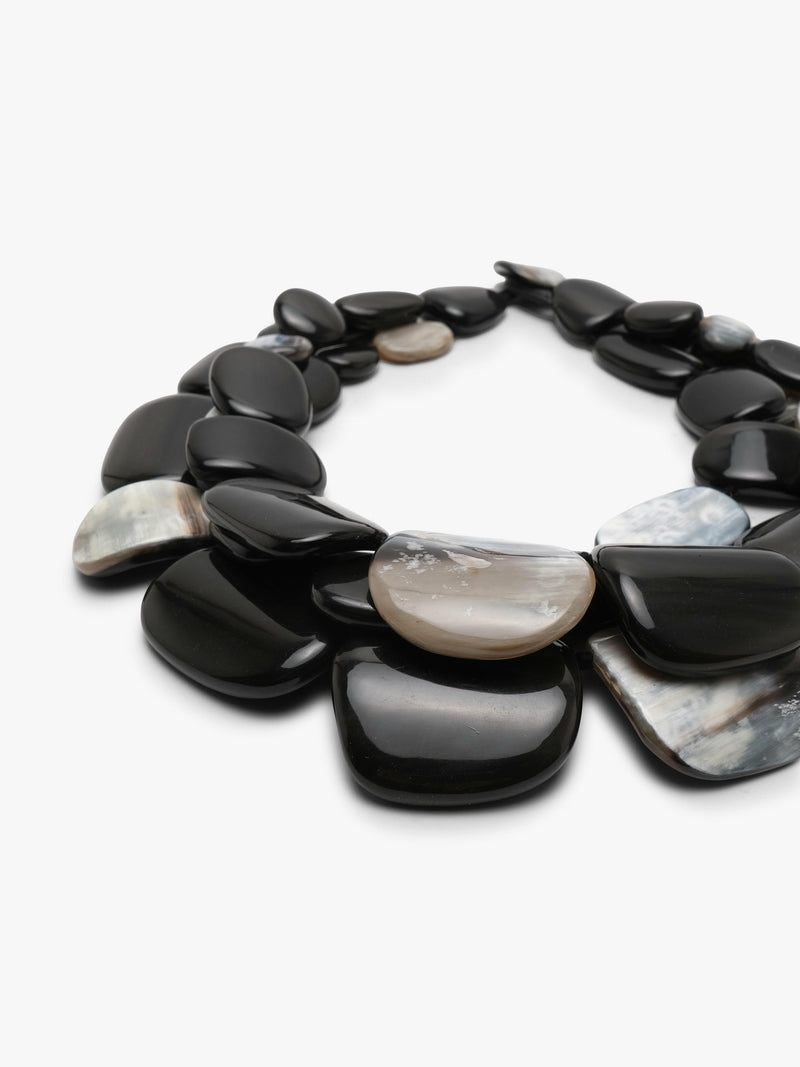 A statement collar necklace made of polished, smooth pebble-shaped horn in black, dark gray with iridescent white and gray patterns, displayed on a clean white background.