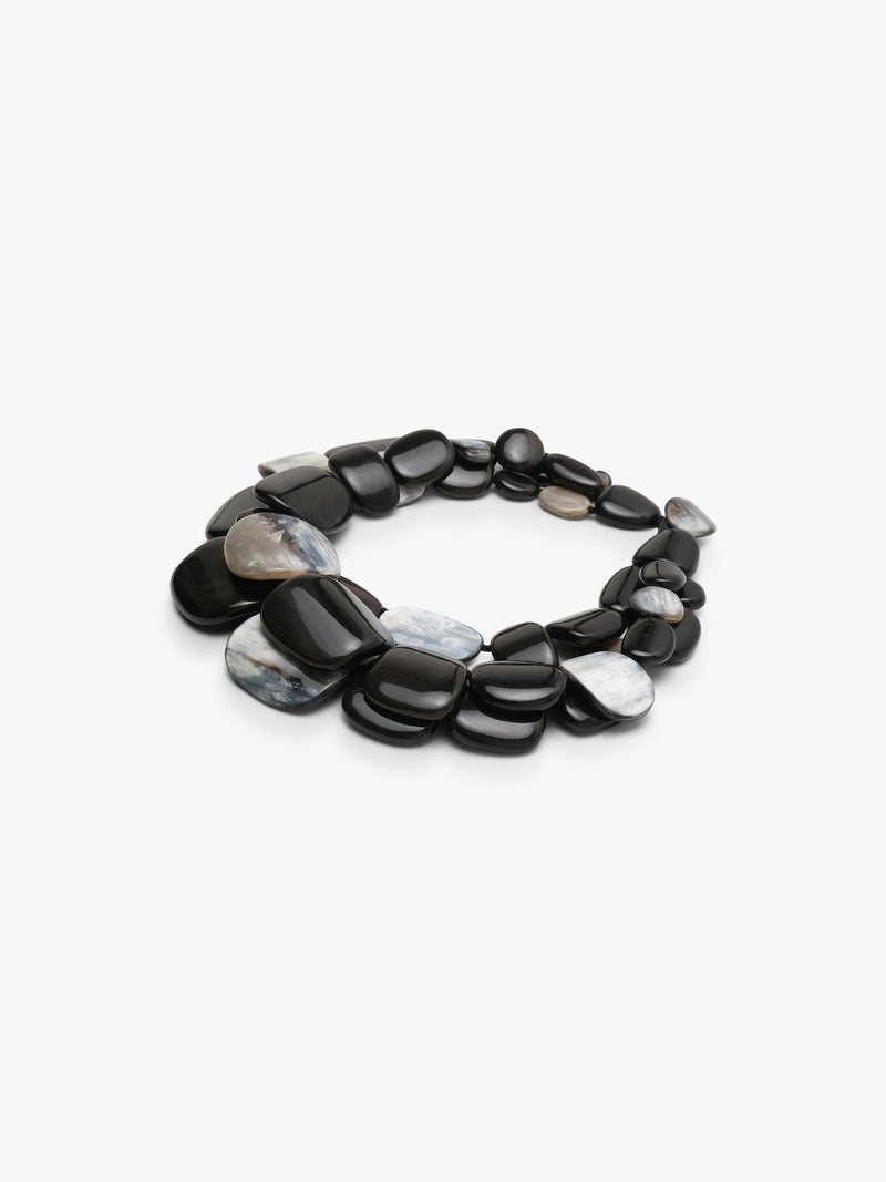 A statement collar necklace made of polished, smooth pebble-shaped horn in black, dark gray with iridescent white and gray patterns, displayed on a clean white background.