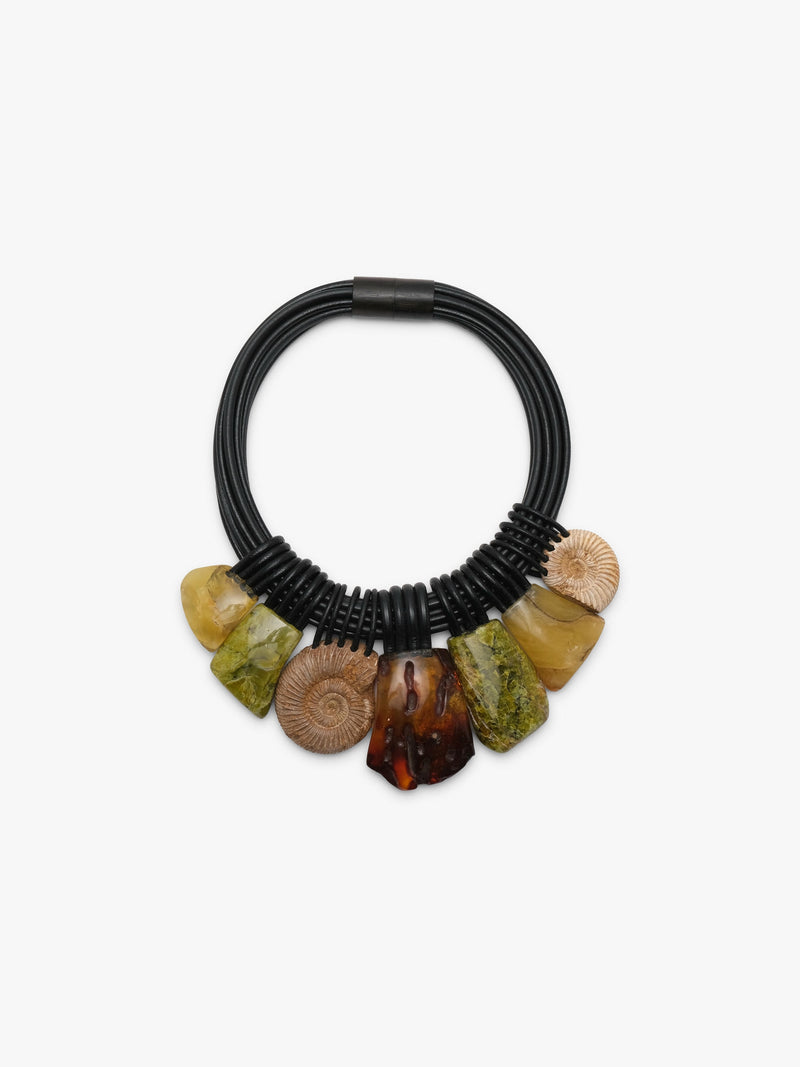 A close up of a black leather necklace, with natural stone beads in brown, green and yellow colours, displayed on a white background.