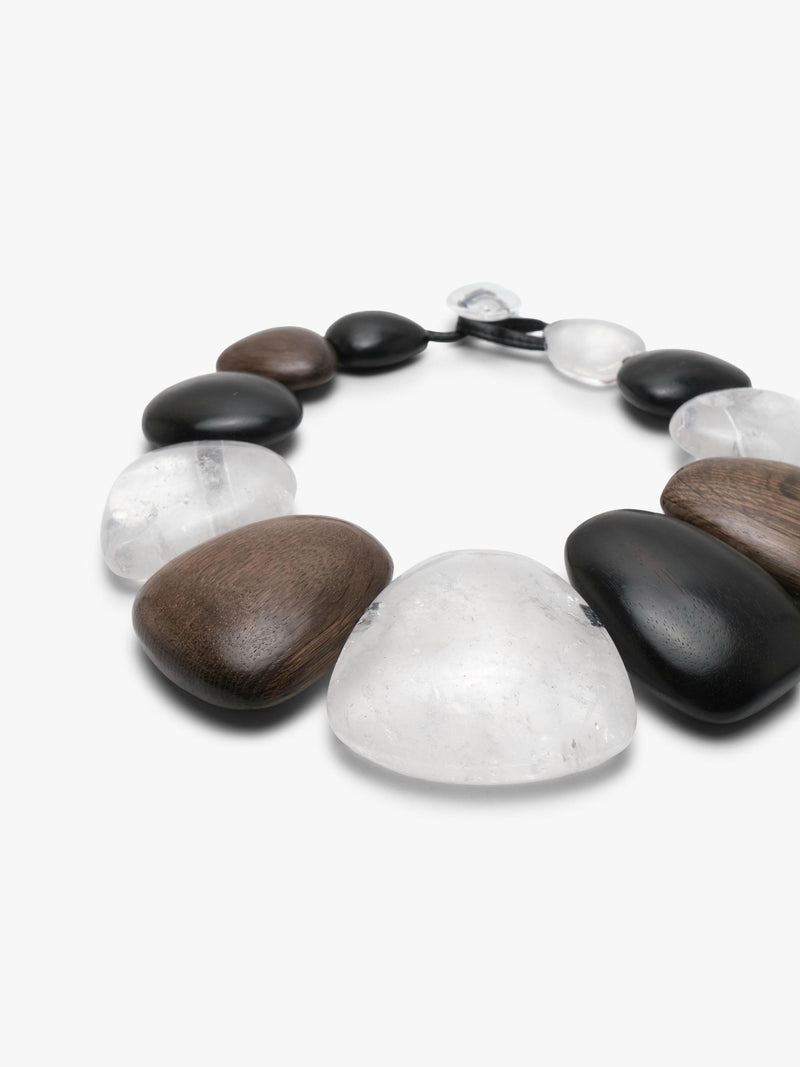 A beaded necklace featuring a mix of smooth black, matte brown, and polished clear stone beads, arranged in a circle on a light gray background.