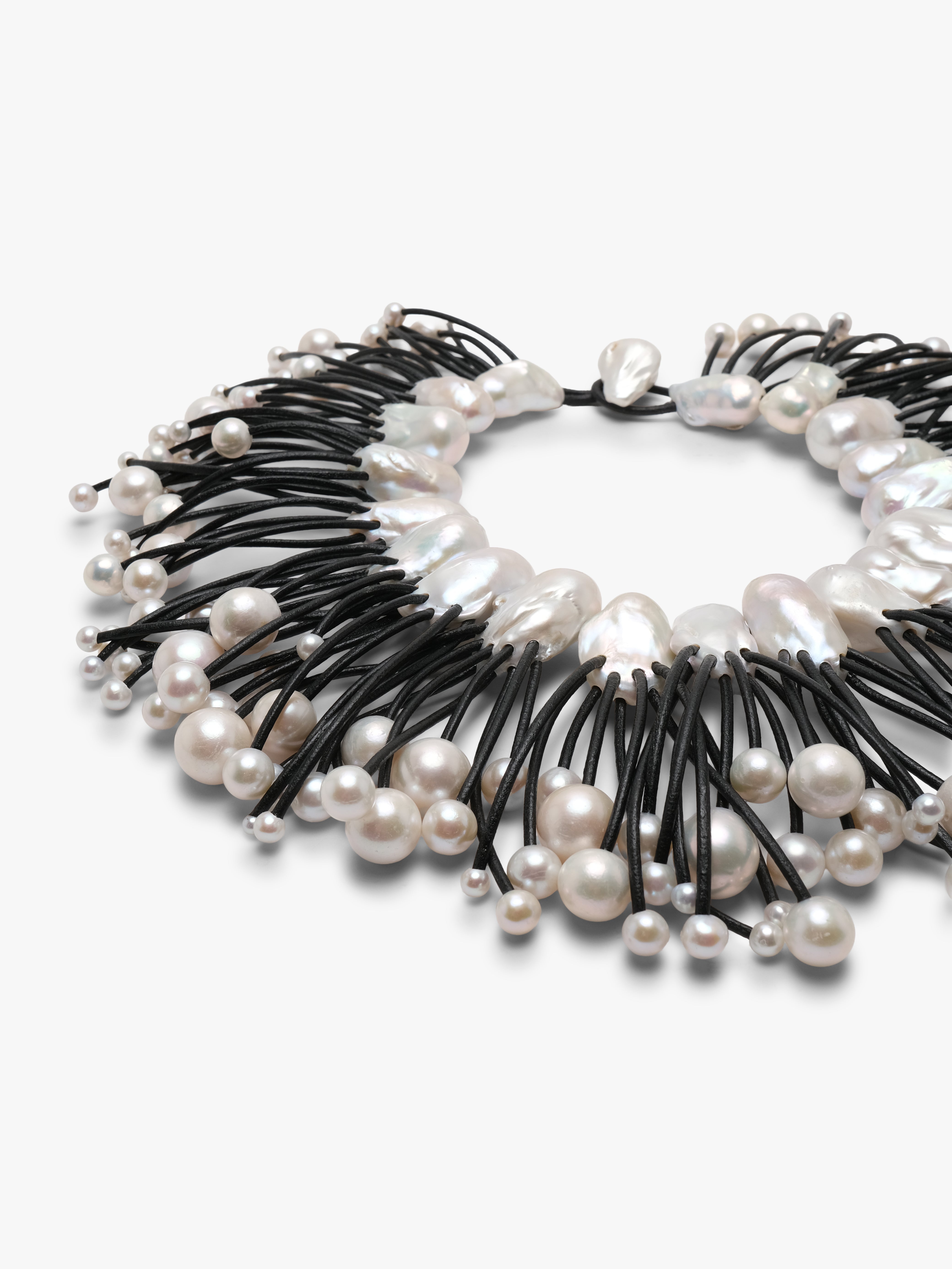 A statement collar necklace featuring irregular white baroque pearls and small silver beads strung along black cords, displayed on a clean white background.