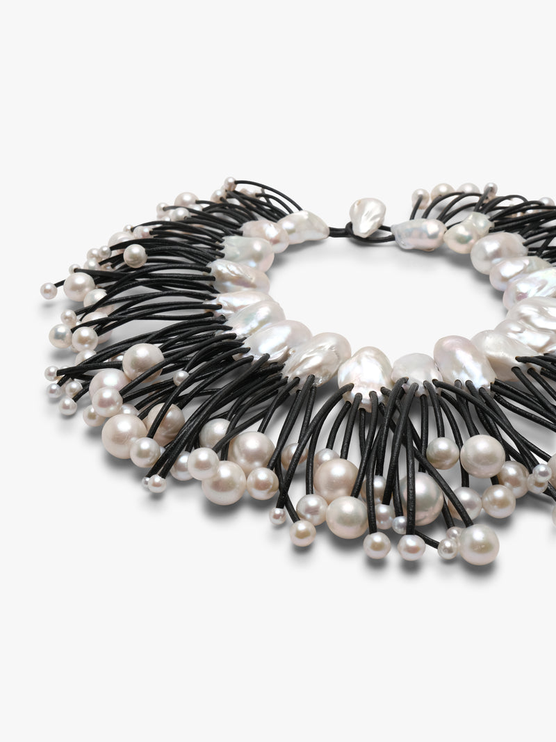 A statement collar necklace featuring irregular white baroque pearls and small silver beads strung along black cords, displayed on a clean white background.