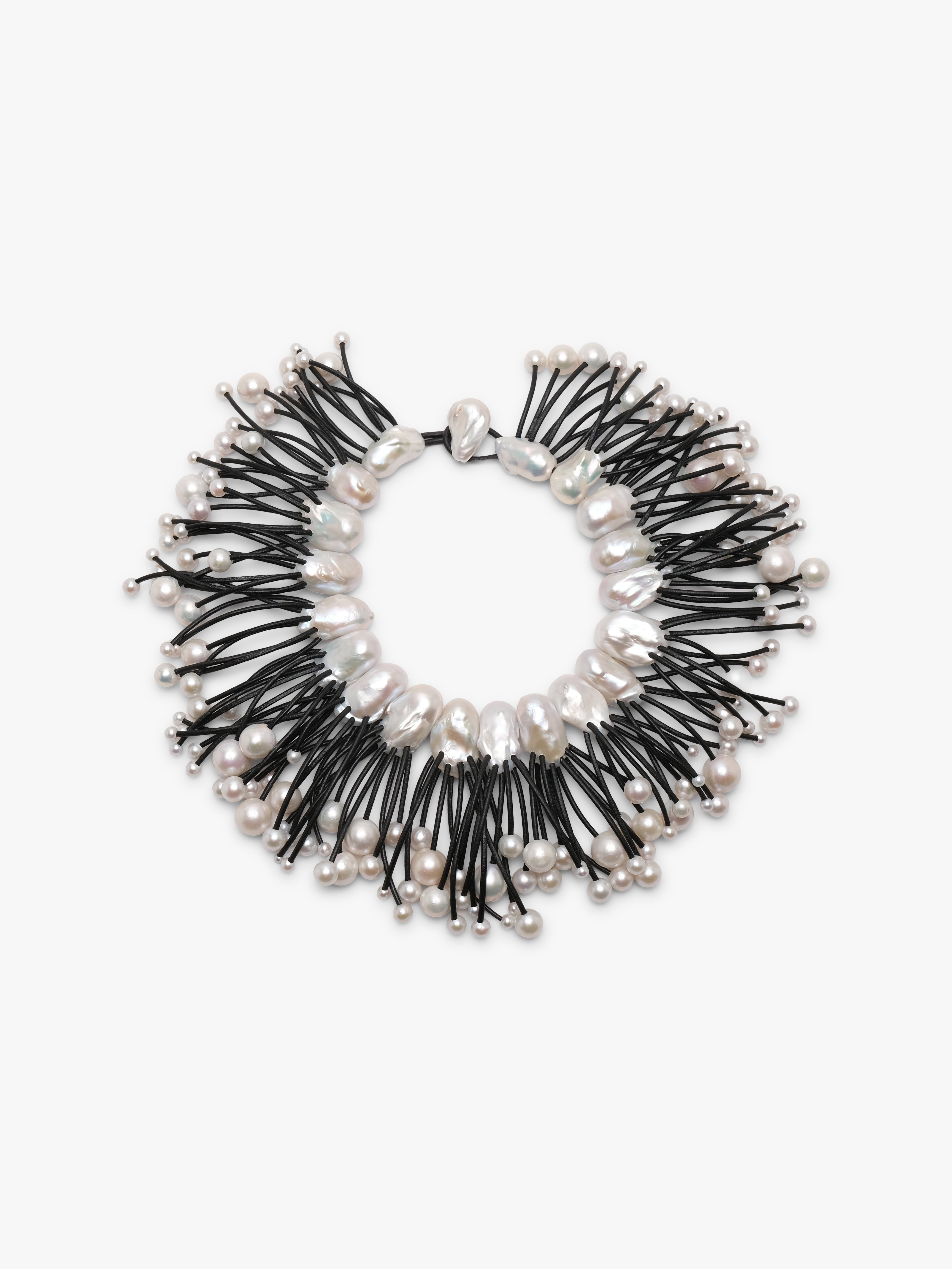 A statement collar necklace featuring irregular white baroque pearls and small silver beads strung along black cords, displayed on a clean white background.