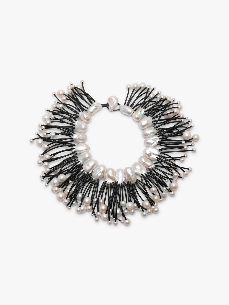 A statement collar necklace featuring irregular white baroque pearls and small silver beads strung along black cords, displayed on a clean white background.