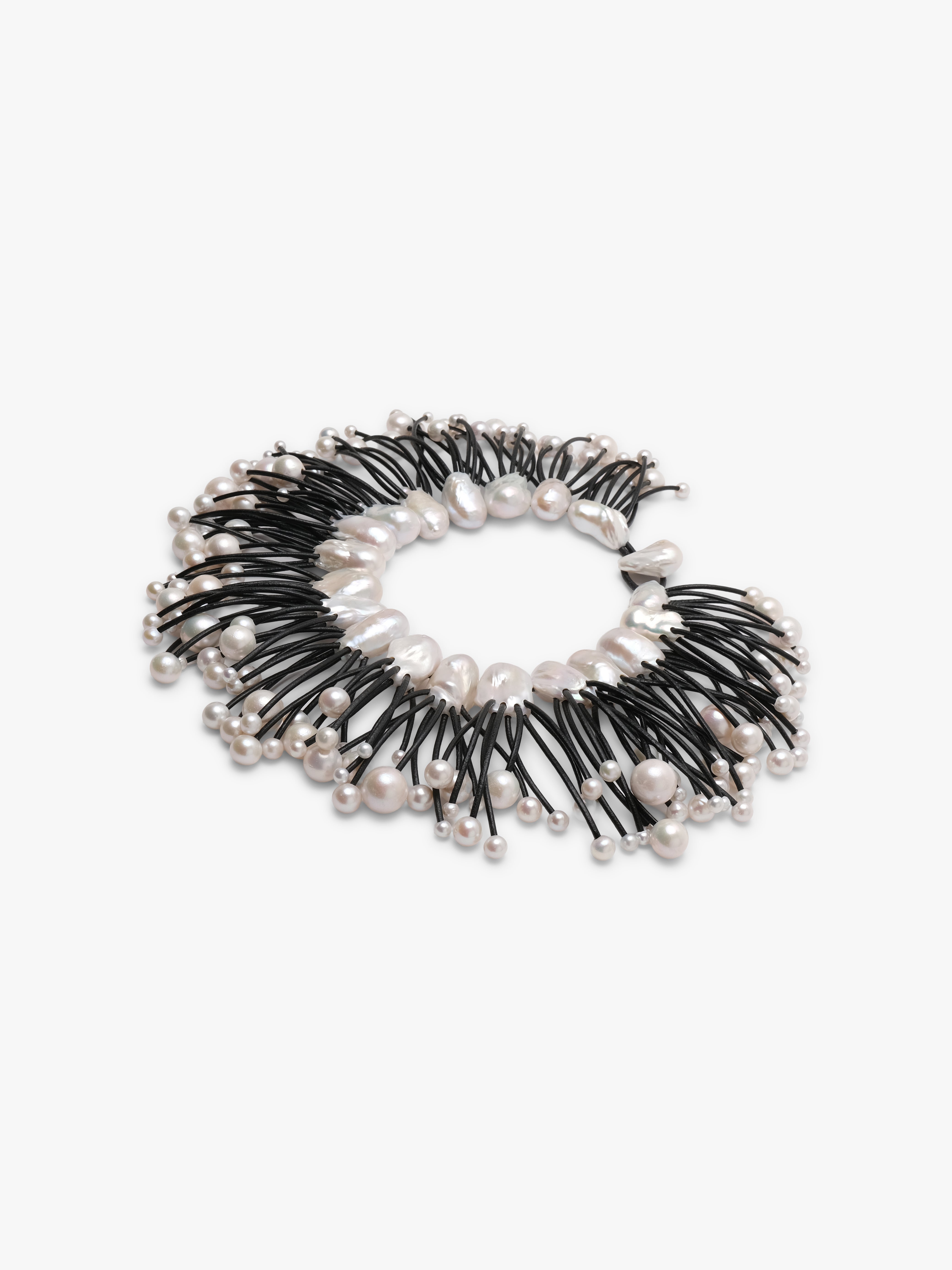 A statement collar necklace featuring irregular white baroque pearls and small silver beads strung along black cords, displayed on a clean white background.
