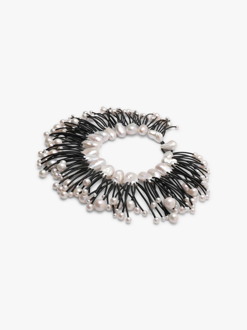 A statement collar necklace featuring irregular white baroque pearls and small silver beads strung along black cords, displayed on a clean white background.