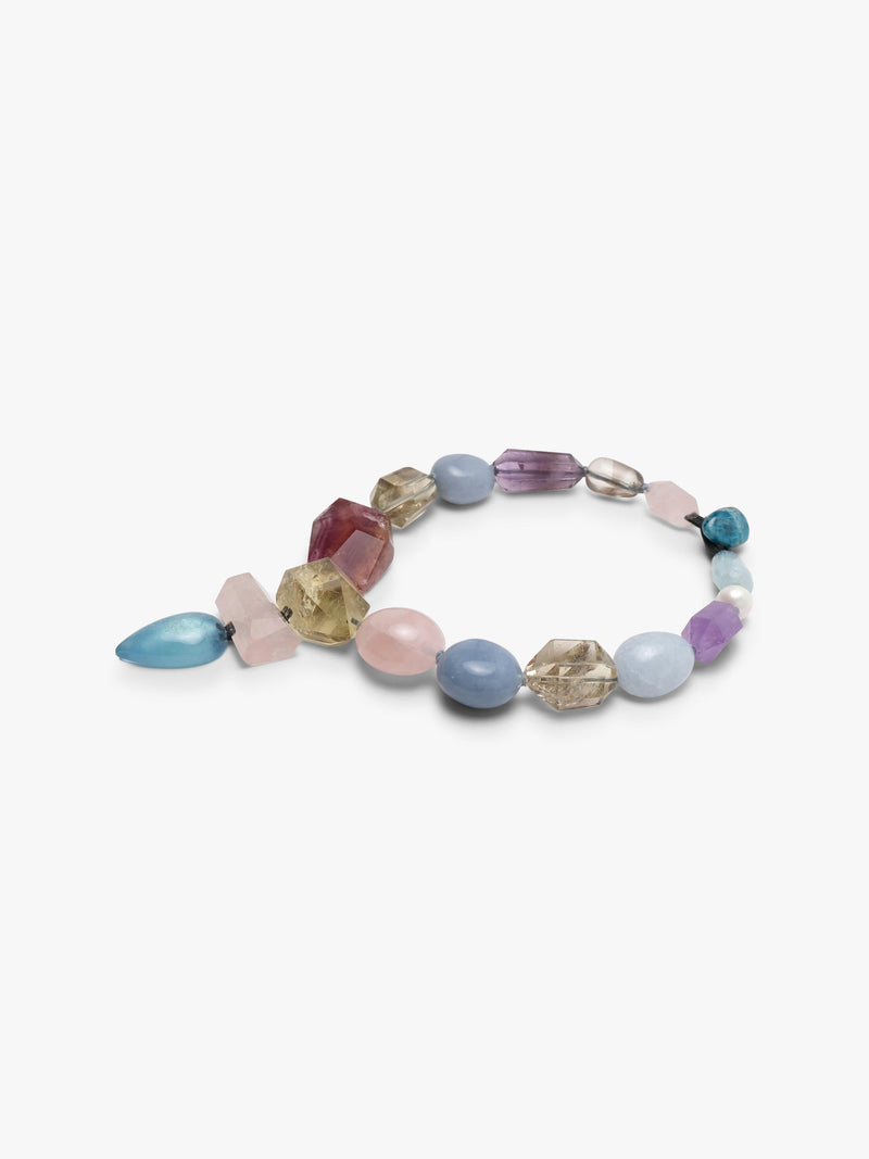 A multicolor beaded necklace featuring faceted gemstone beads in shades of pink, light blue, purple, amber, and clear, with a teardrop-shaped light blue stone pendant hanging from the center, set against a plain white background.