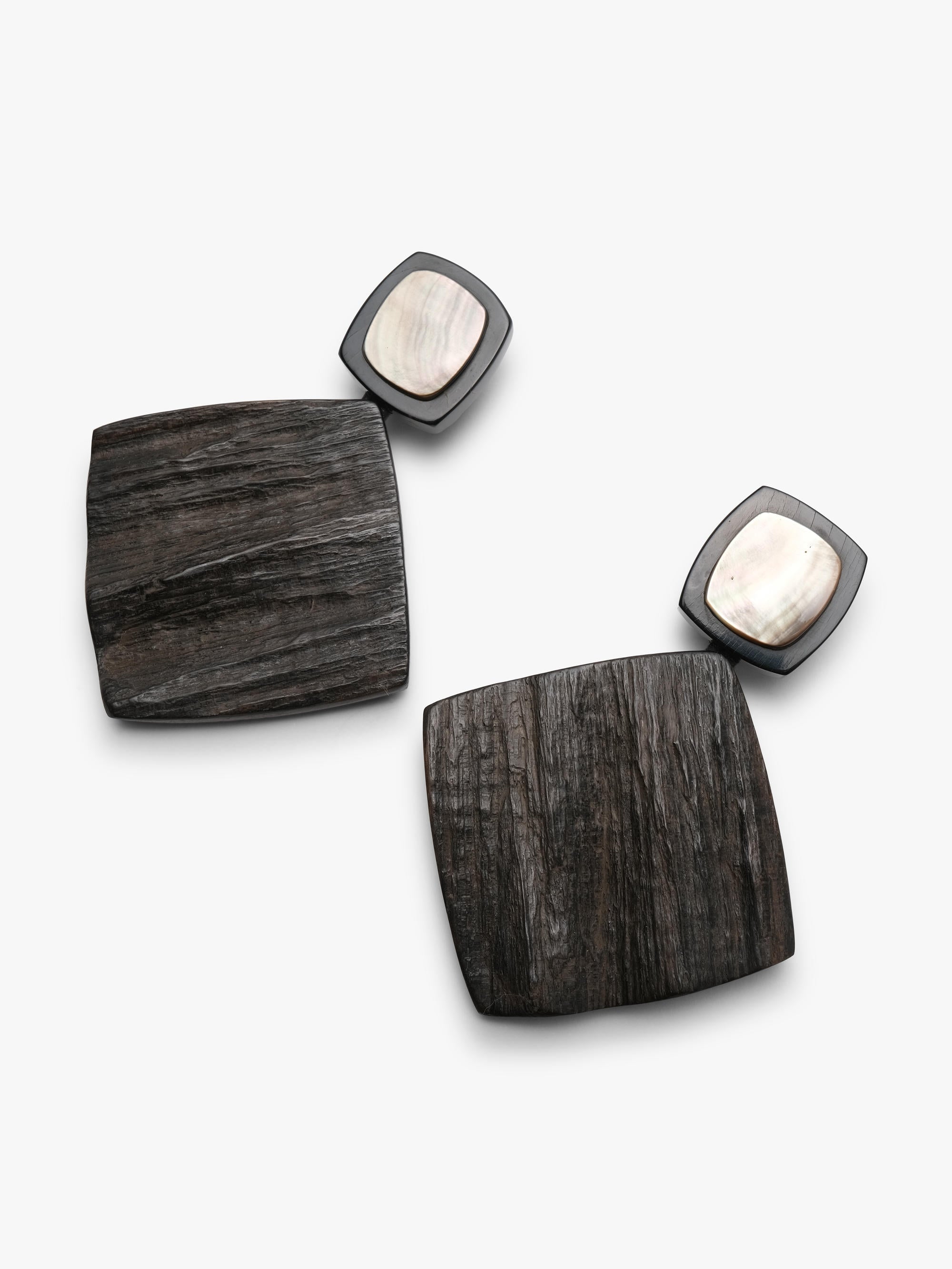 A pair of statement earrings featuring large, dark horn-grain square pendants with rounded corners and small, dark-framed oval studs with light mother-of-pearl centers, shown on a clean white background.
