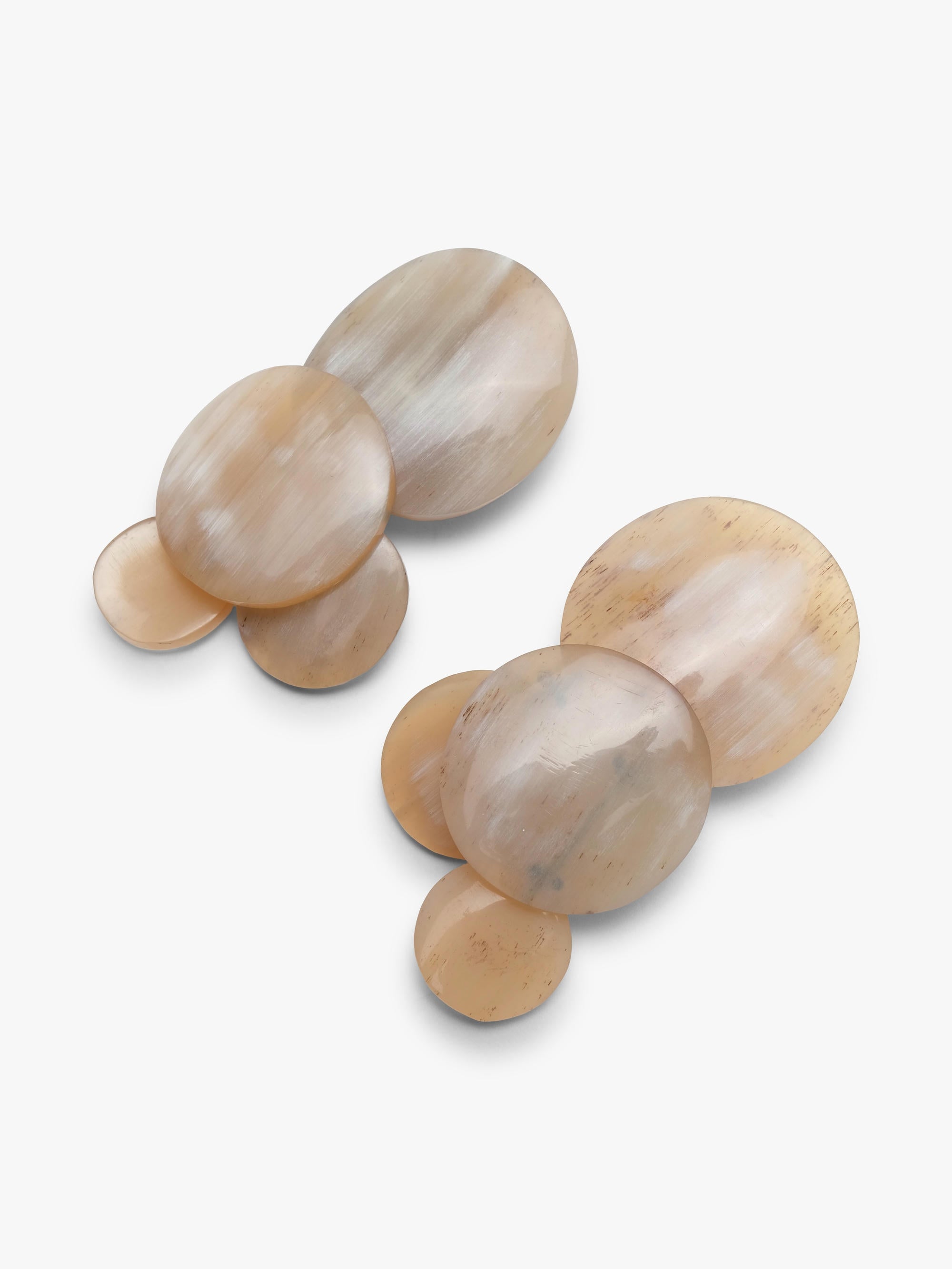 A pair of statement earrings made of multiple organic-shaped horn discs in a pearlescent champagne beige color, arranged on a clean white background.