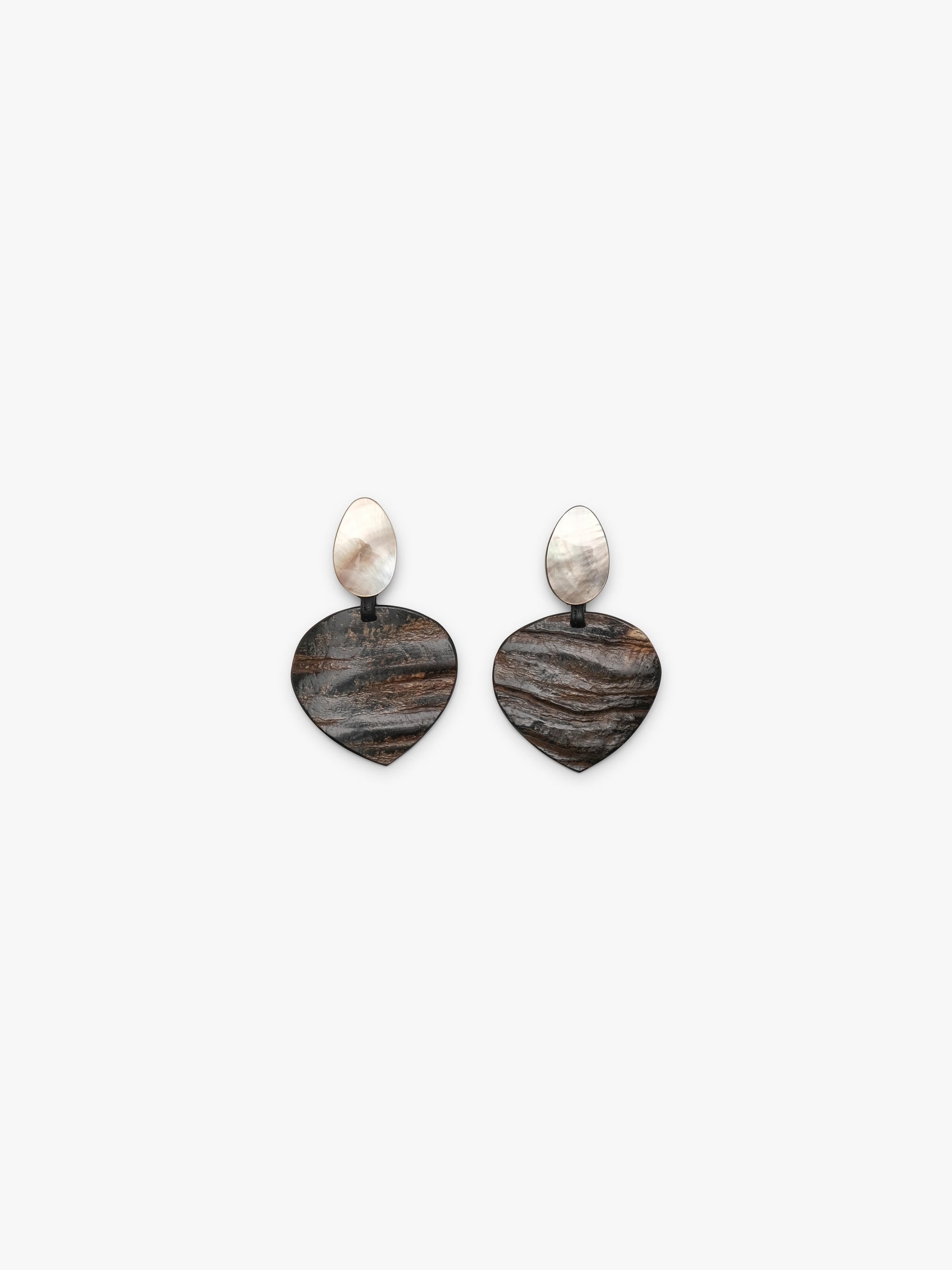 A pair of drop earrings featuring textured, dark brown and black horn-grain heart-shaped pendants with smooth, pear-shaped white mother-of-pearl studs on a light gray background.