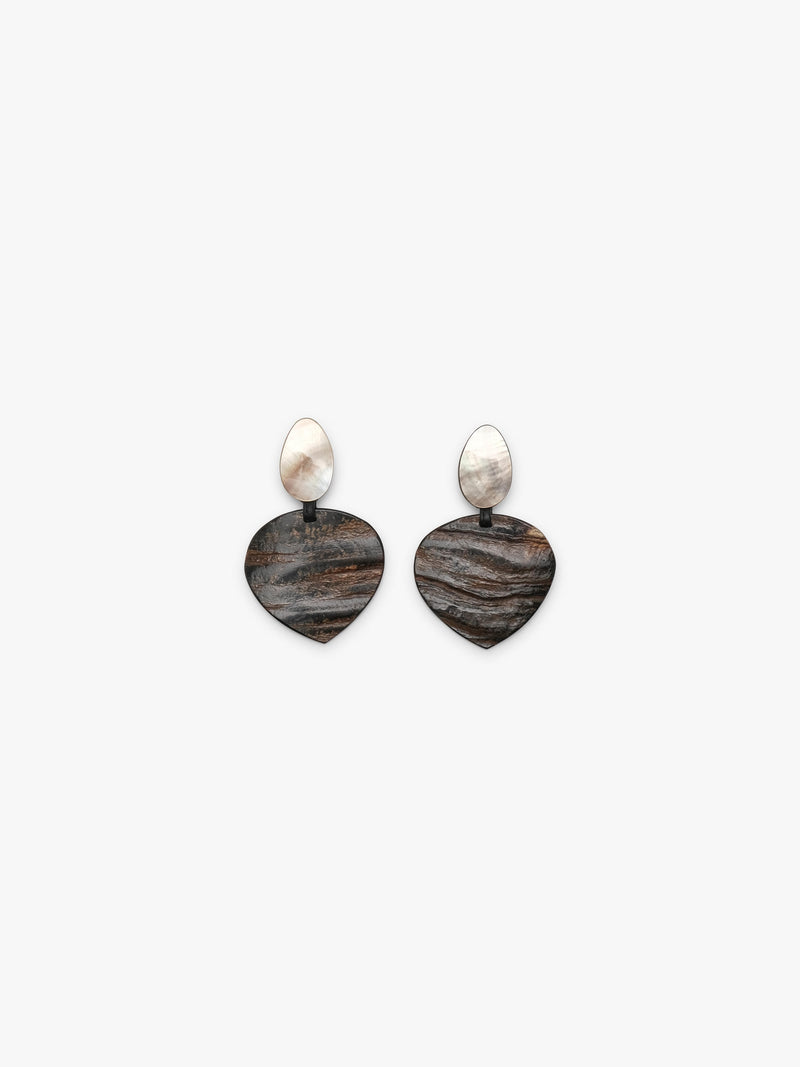 A pair of drop earrings featuring textured, dark brown and black horn-grain heart-shaped pendants with smooth, pear-shaped white mother-of-pearl studs on a light gray background.