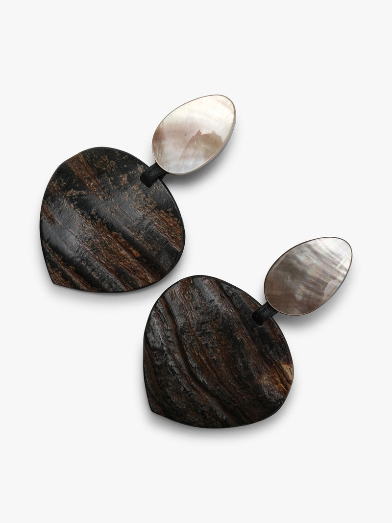 A pair of drop earrings featuring textured, dark brown and black horn-grain heart-shaped pendants with smooth, pear-shaped white mother-of-pearl studs on a light gray background.