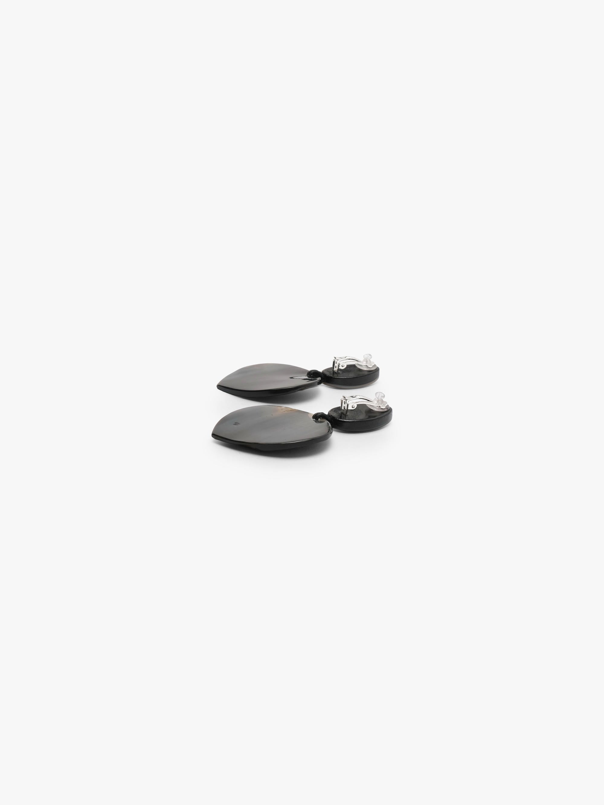 A pair of drop earrings featuring textured, dark brown and black horn-grain heart-shaped pendants with smooth, pear-shaped white mother-of-pearl studs on a light gray background.