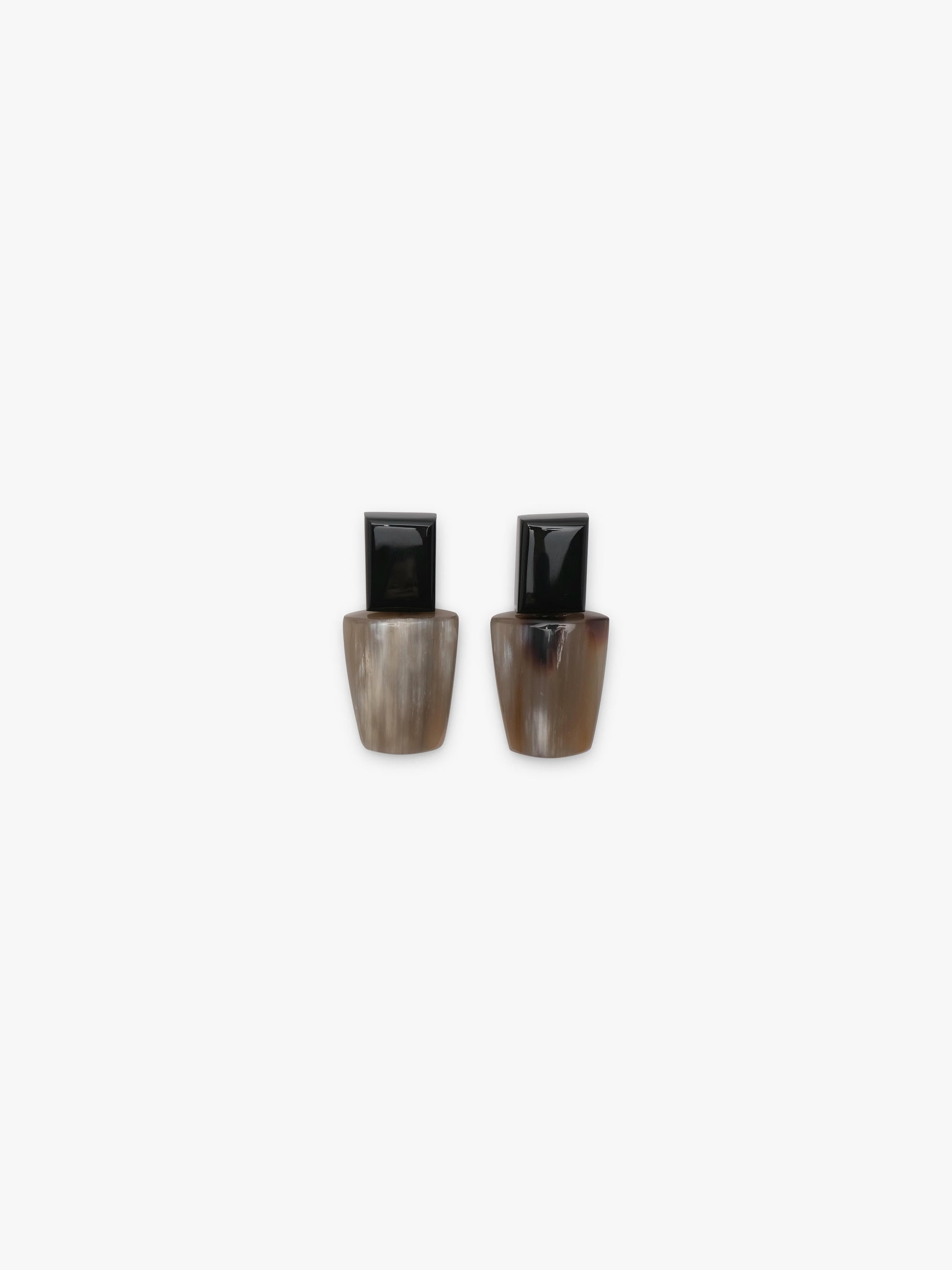 A pair of earrings with a black top and a greyish brown bottom, displayed on a white background